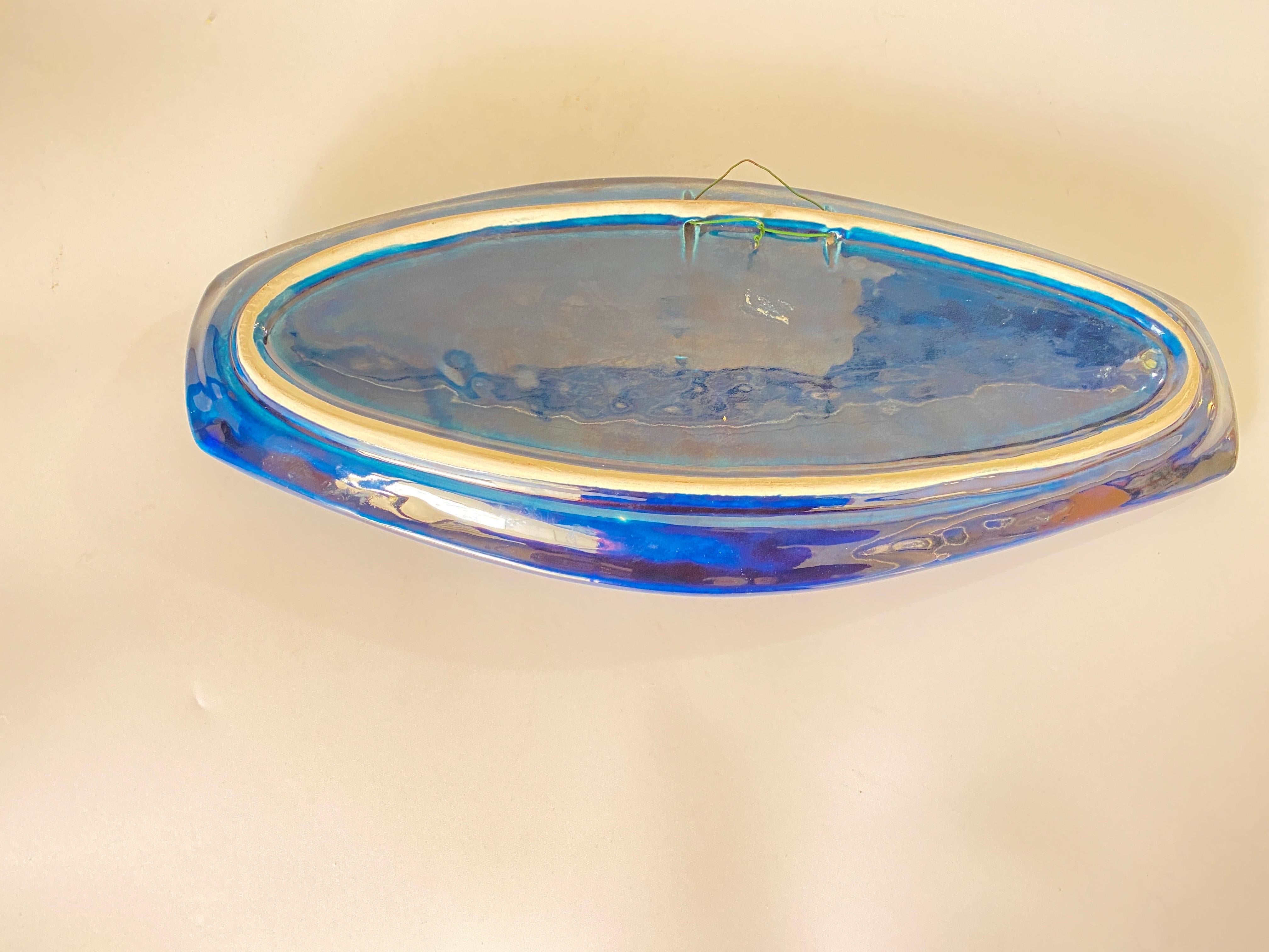 Se trata de una cerámica mayólica para la decoración. Se fabricó en Francia en la década de 1960. Sus colores son el azul, el verde y el naranja.
