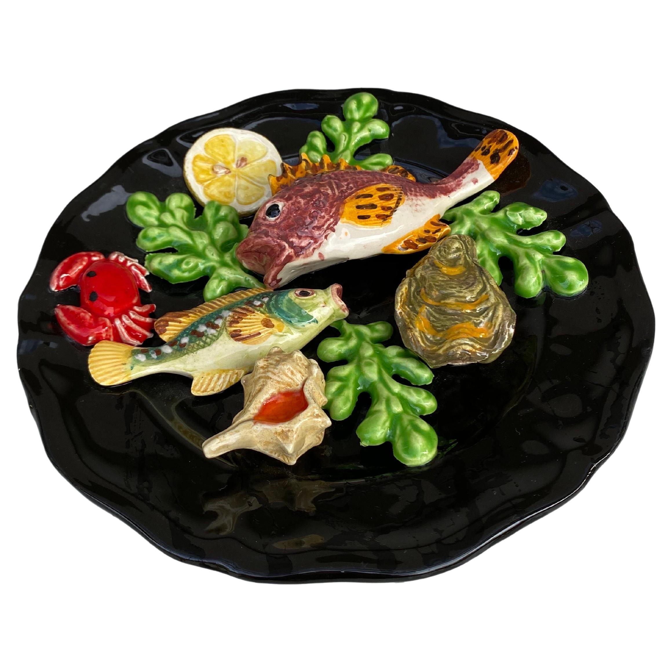 Plato de mayólica Vallauris, hacia 1950.
Altorrelieve de 2 peces, algas, limón, estrella de mar, conchas, cangrejo, ostra.
Estilo náutico.
Medida: 9,3 de diámetro.
 