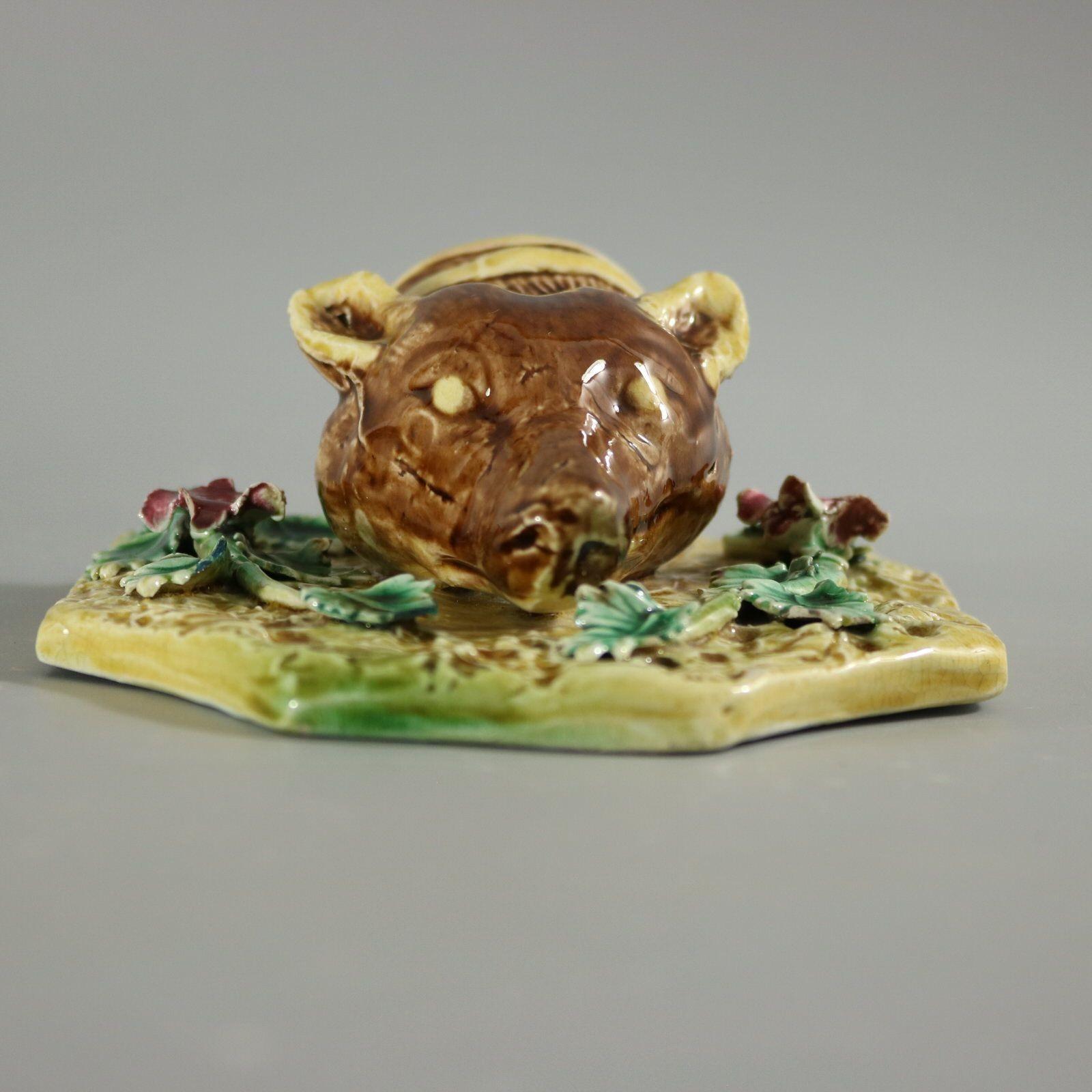 Tasca da parete in maiolica che presenta il modello di una staffa a testa di volpe, seduta su un fondo sagomato, con fiori ai lati. Colorazione: predominano il giallo, il marrone e il verde.