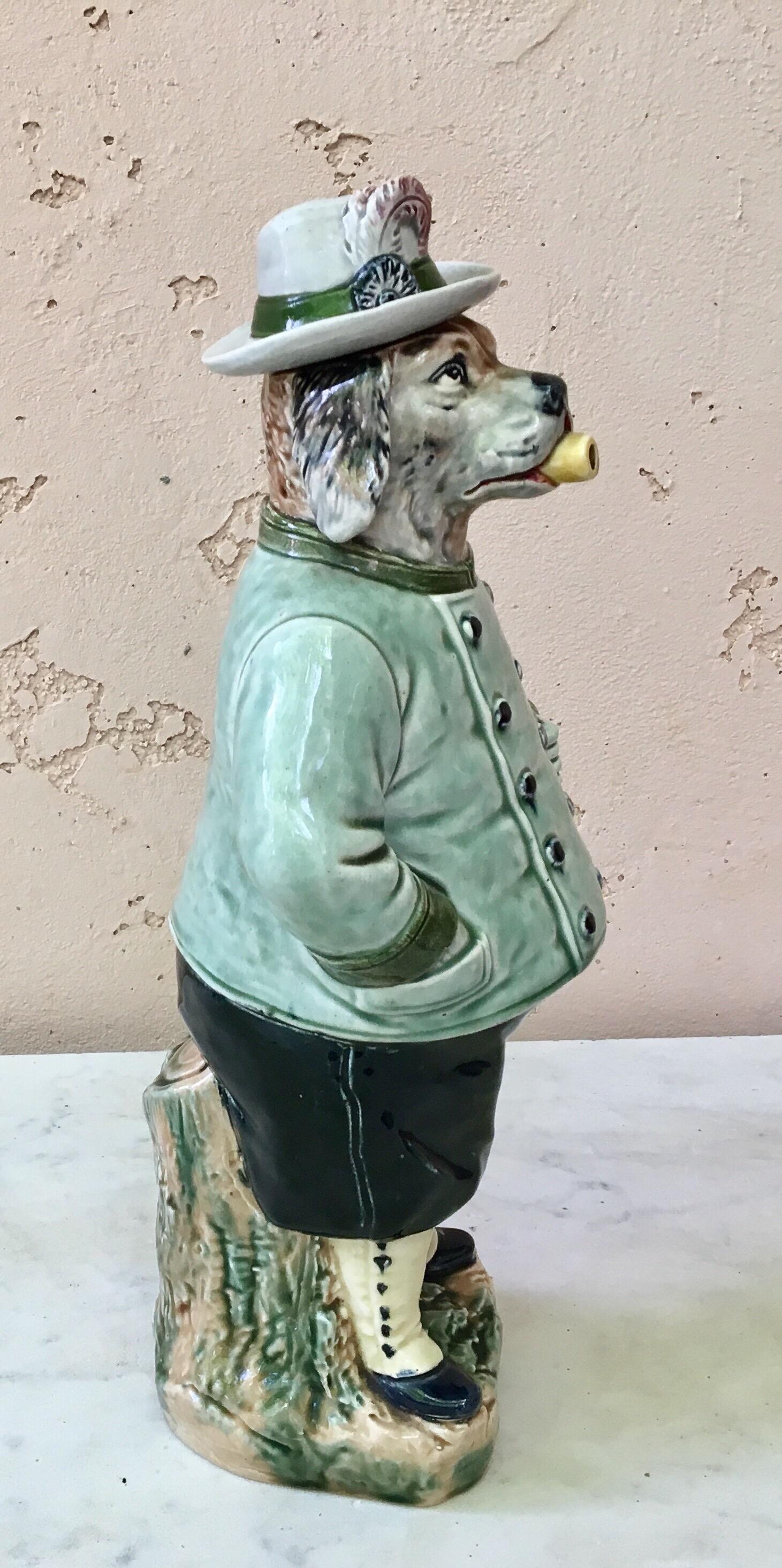 Majolica German figural dog bottle, circa 1890.
The bottle represent a dog in hunting costume smoking a pipe and carrying a riffle, the lid is the hat with a feather.
The piece is signed B.L geselzl-gesch number 2343.