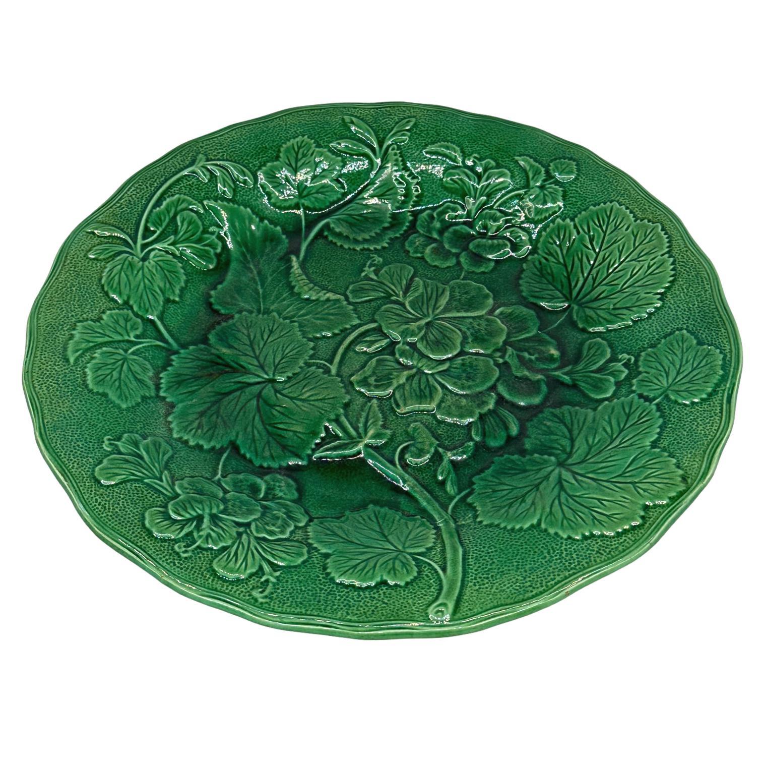 Assiette de 9,13 pouces en majolique anglaise à glaçure verte, avec des plantes et des fleurs de géranium moulées en relief et un bord façonné, par la firme anglaise Hope & Carter, Burslem, Stoke-on-Trent, vers les années 1870.  Revers avec le