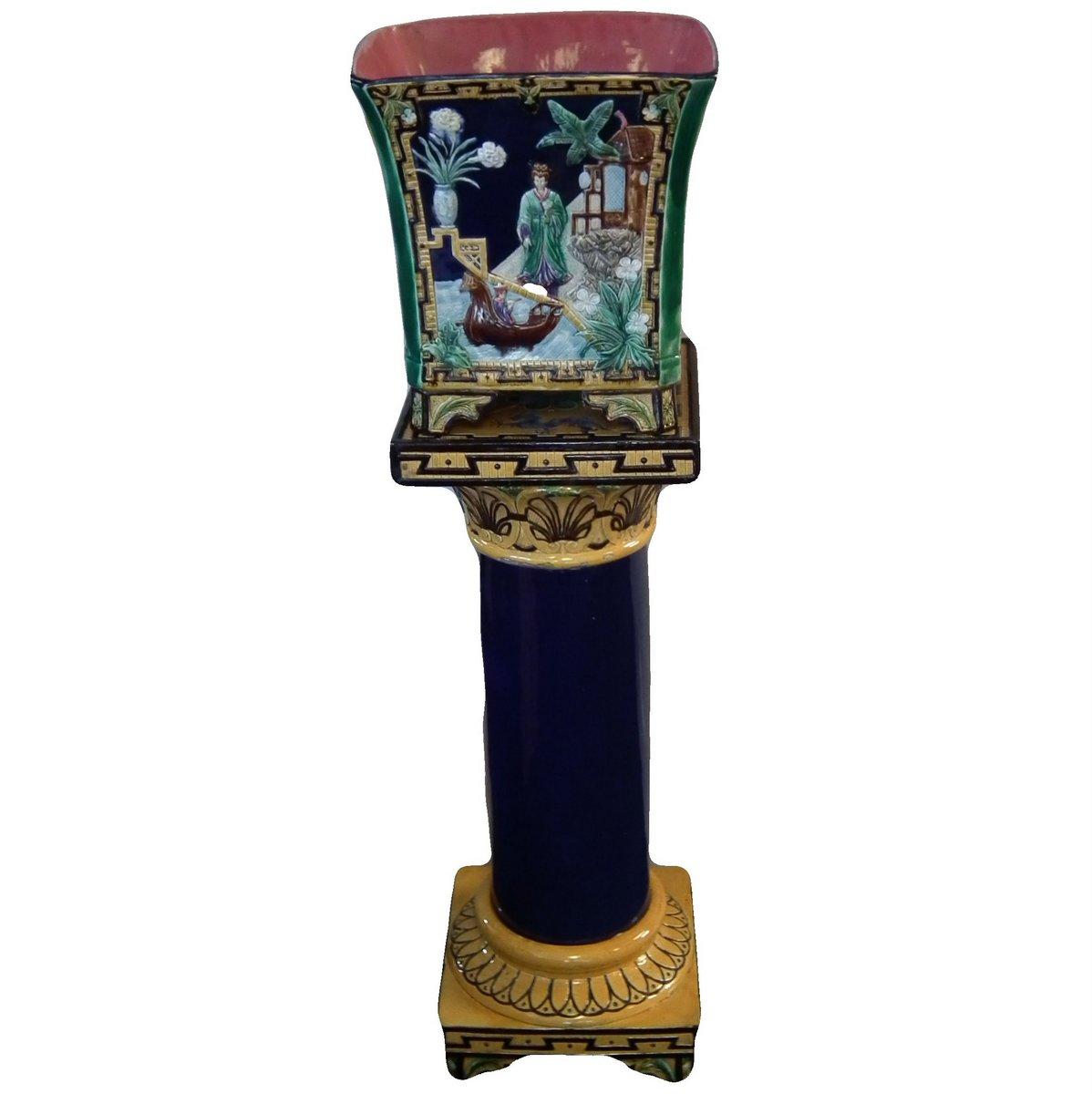Majolica jardinière and stand which features pictorial panels: Two depicting oriental scenes with figures. The other two with a stork in flight over water. Coloration: ochre, green, white, are predominant.
