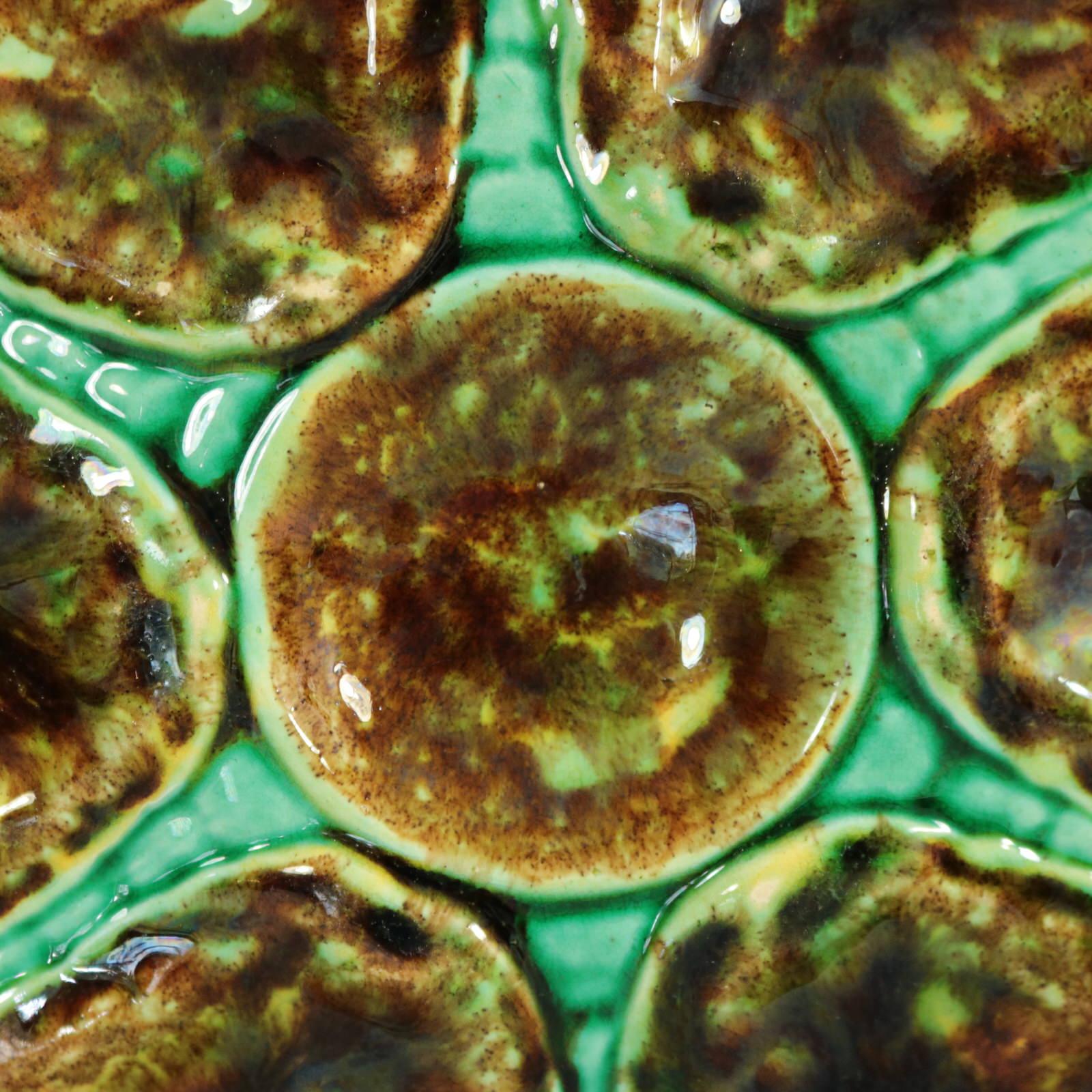 Unidentified English or European Majolica oyster plate which features six shell-shaped wells surrounding a circular central well. Colouration: green, brown, yellow, are predominant. Bears a pattern number, '::'.