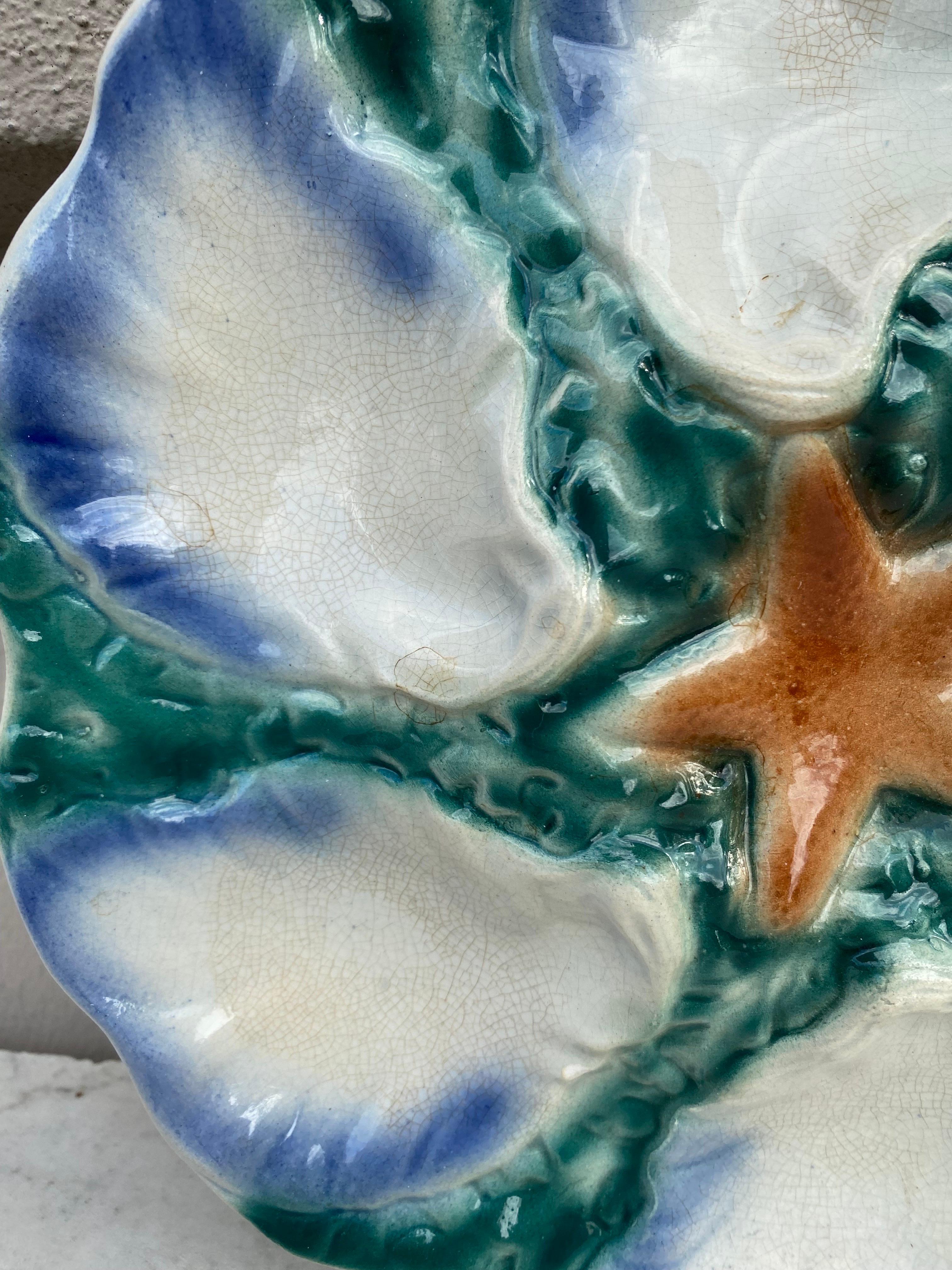 Assiette en majolique avec étoile de mer orange à six godets bleu et blanc entourée d'algues vertes Digoin ( Est de la France ), vers 1900.