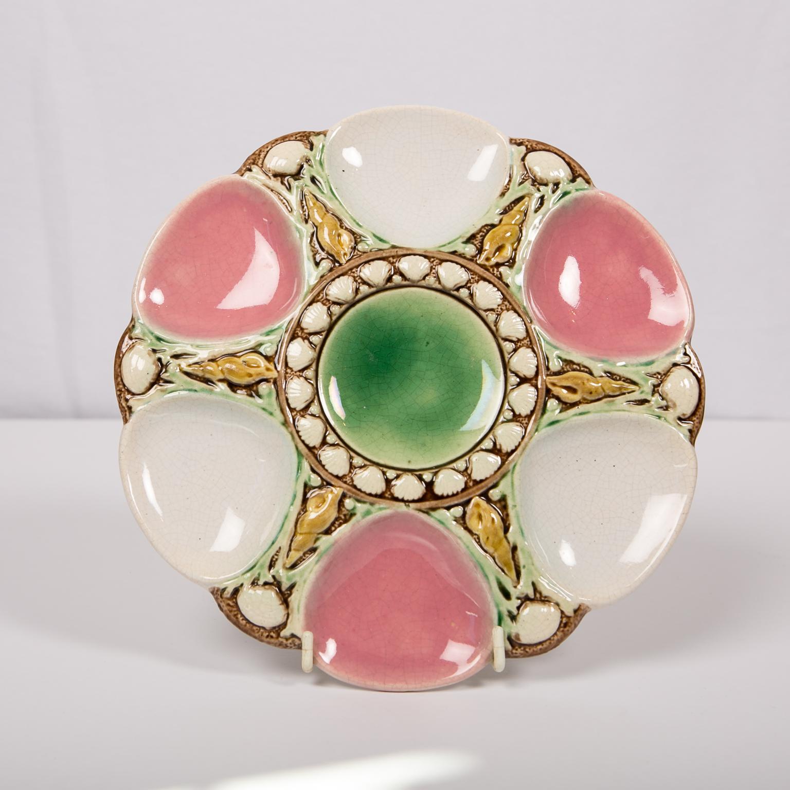 A beautiful Majolica oyster plate painted with colored glazes with three pink and three white oyster cups and a green central rondel for sauce, all enhanced by a decoration of sea shells separating the six cups.
Background
 Oyster plates were first
