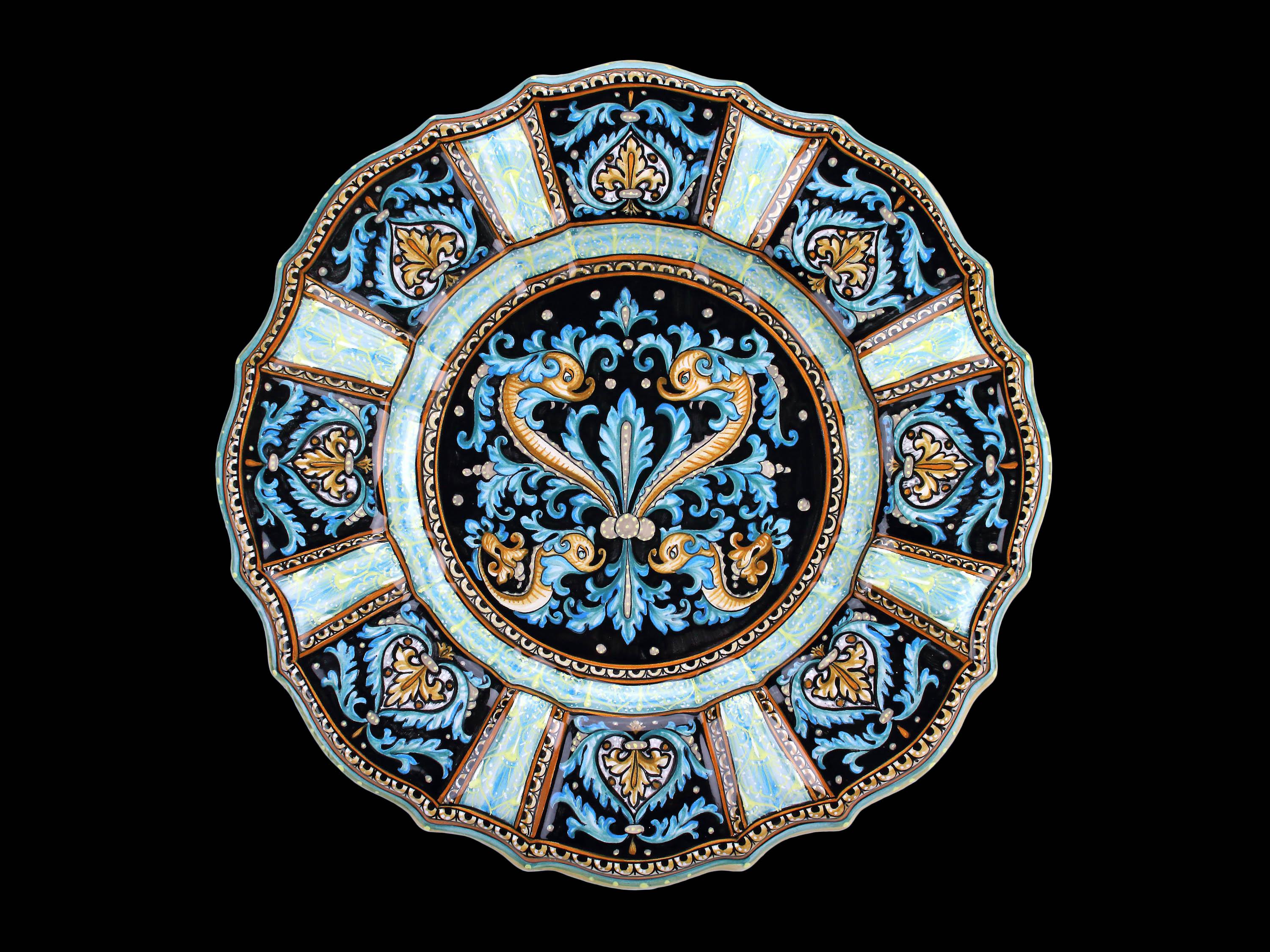 Plat en majolique fabriqué et peint à la main à Deruta, en Italie, selon la technique de peinture originale de la Renaissance. Le plat est enrichi par la présence de quatre figures de dauphins métamorphiques disposées symétriquement ; dans