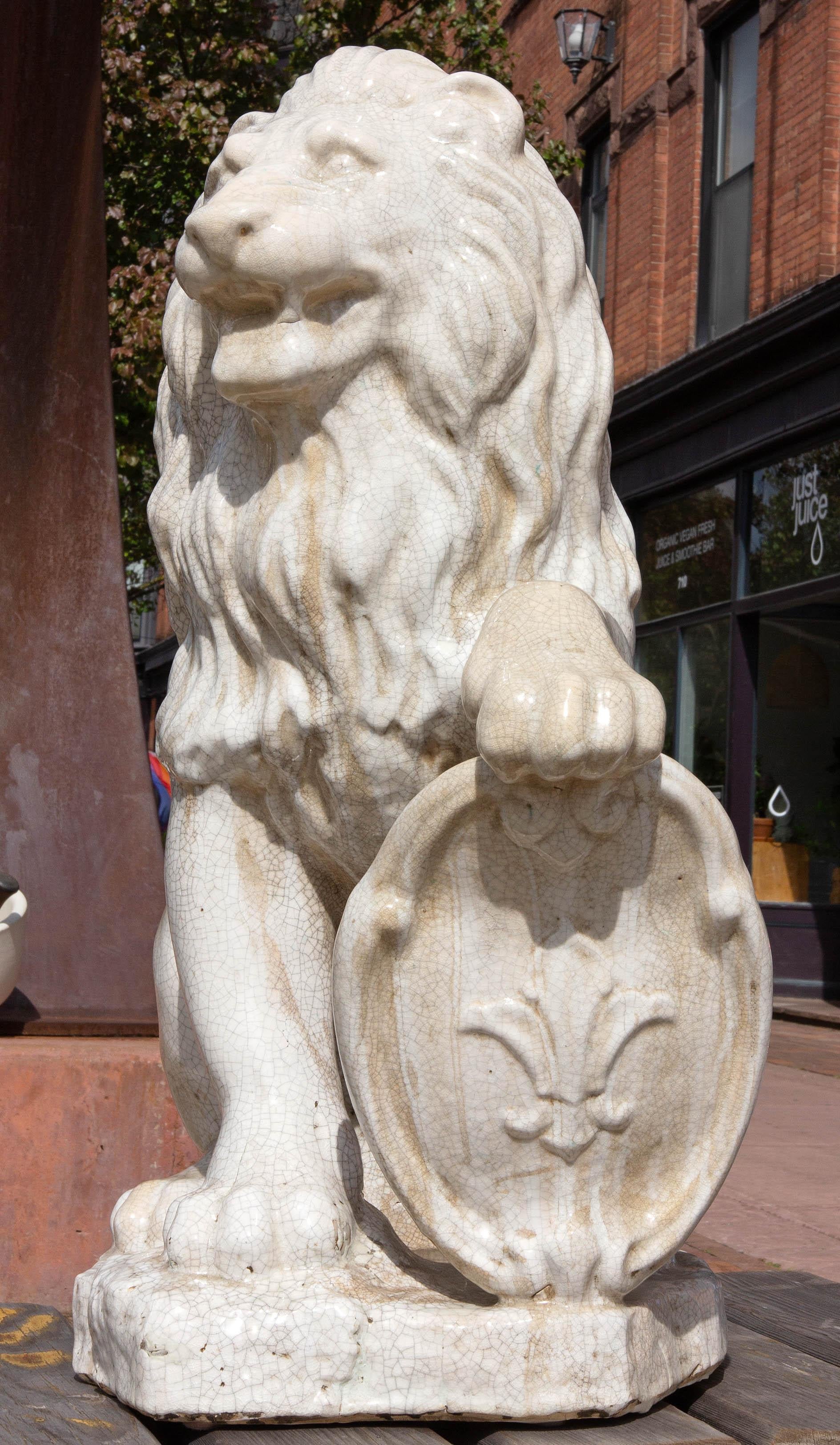 Sitzender Löwe aus Majolika mit weißer Craquelé-Glasur und heraldischem Schild. Schön verwittert mit Bereichen von Mineralablagerungen.