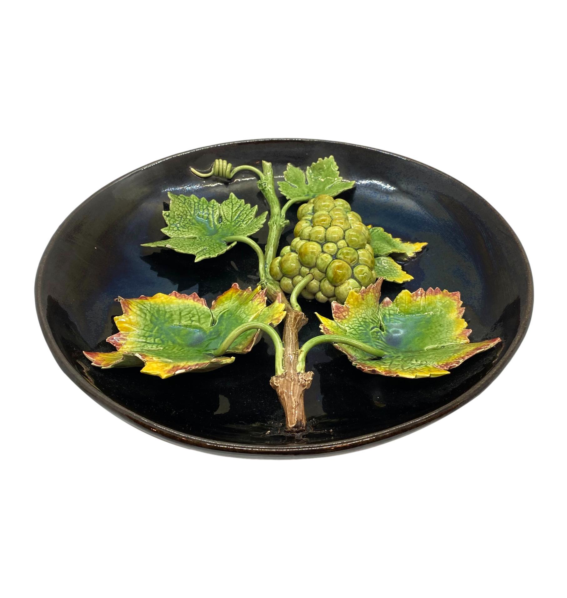 Majolica Trompe l'oeil round plaque, with applied green glazed grapes molded in high relief, with grapevines and vividly glazed grape leaves, on a deep cobalt blue-glazed ground, reverse with impressed mark for Rafael Bordalo Pinheiro (1846-1905),