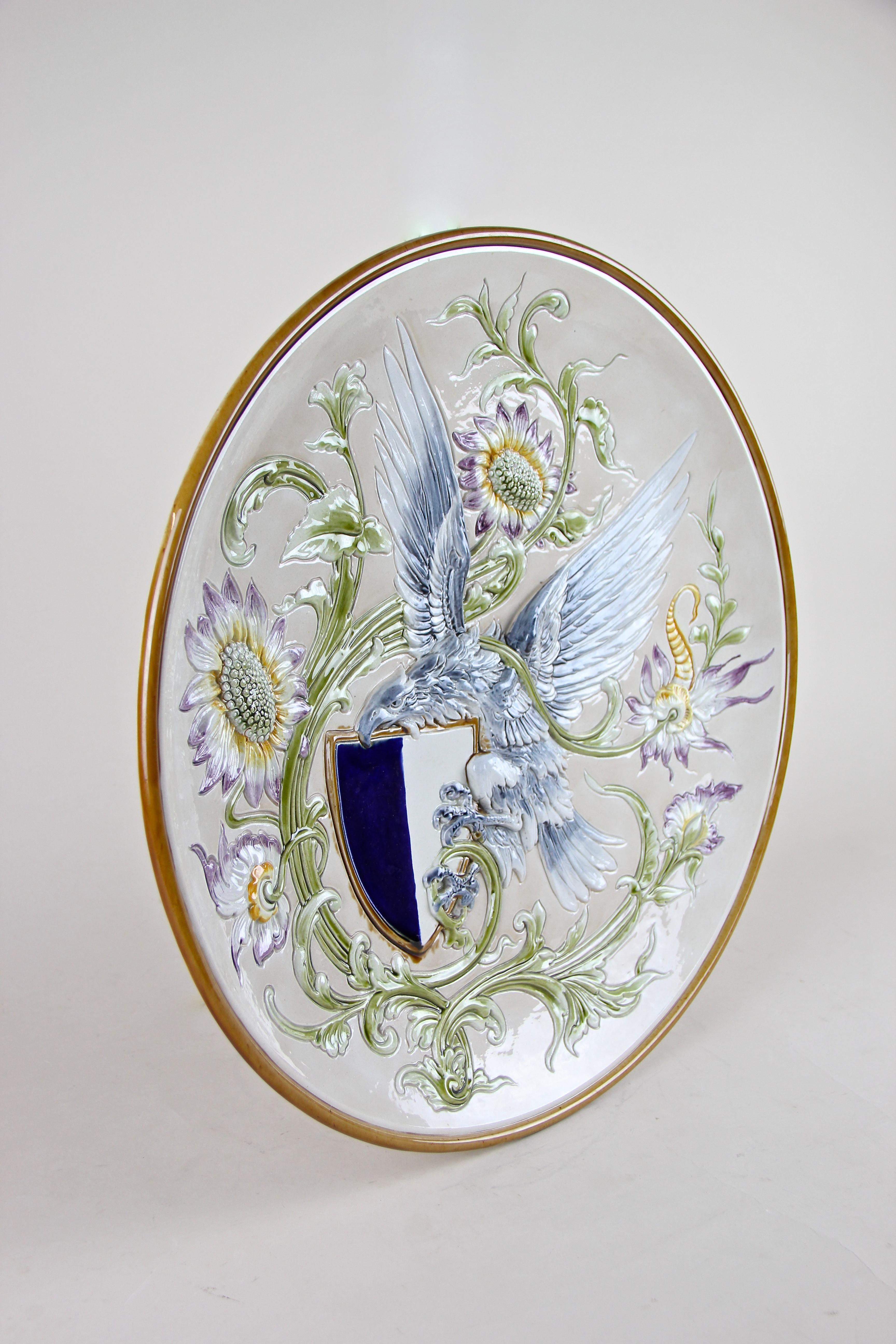 Outstanding Majolica wall plate out of the famous workshops of Wilhelm Schiller & Son in Bohemia from around 1890. Adorned by a fantastic worked blue eagle holding a blue/white coat of arms surrounded by a gorgeous floral design in relief this late