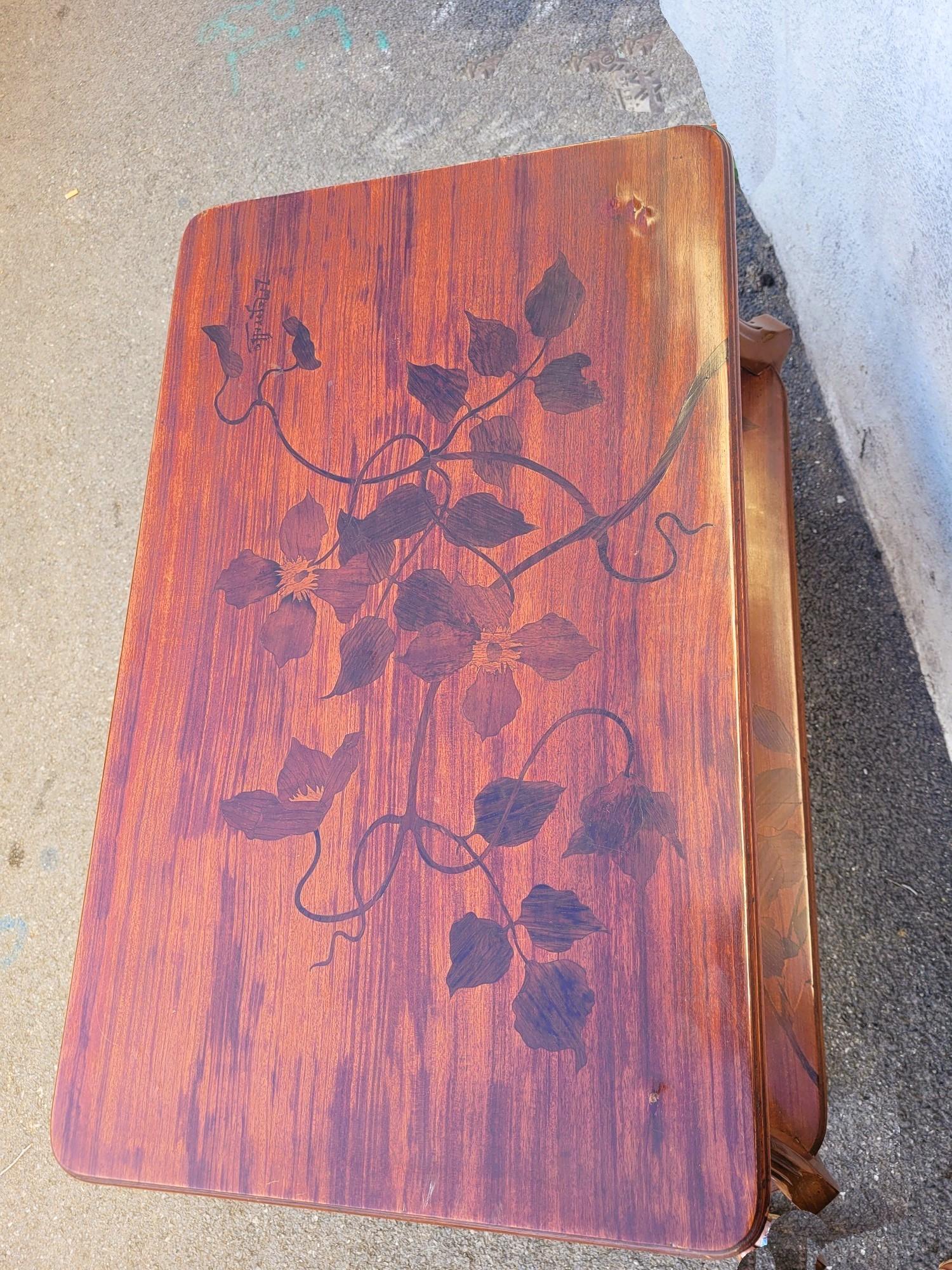 Table à thé avec 2 plateaux, en marqueterie de différentes essences de bois : les plateaux sont décorés de fleurs (clématites) et de feuilles, le plateau supérieur est signé I.L.A.

Il est également décoré de 2 poignées en bronze

Bon état général,