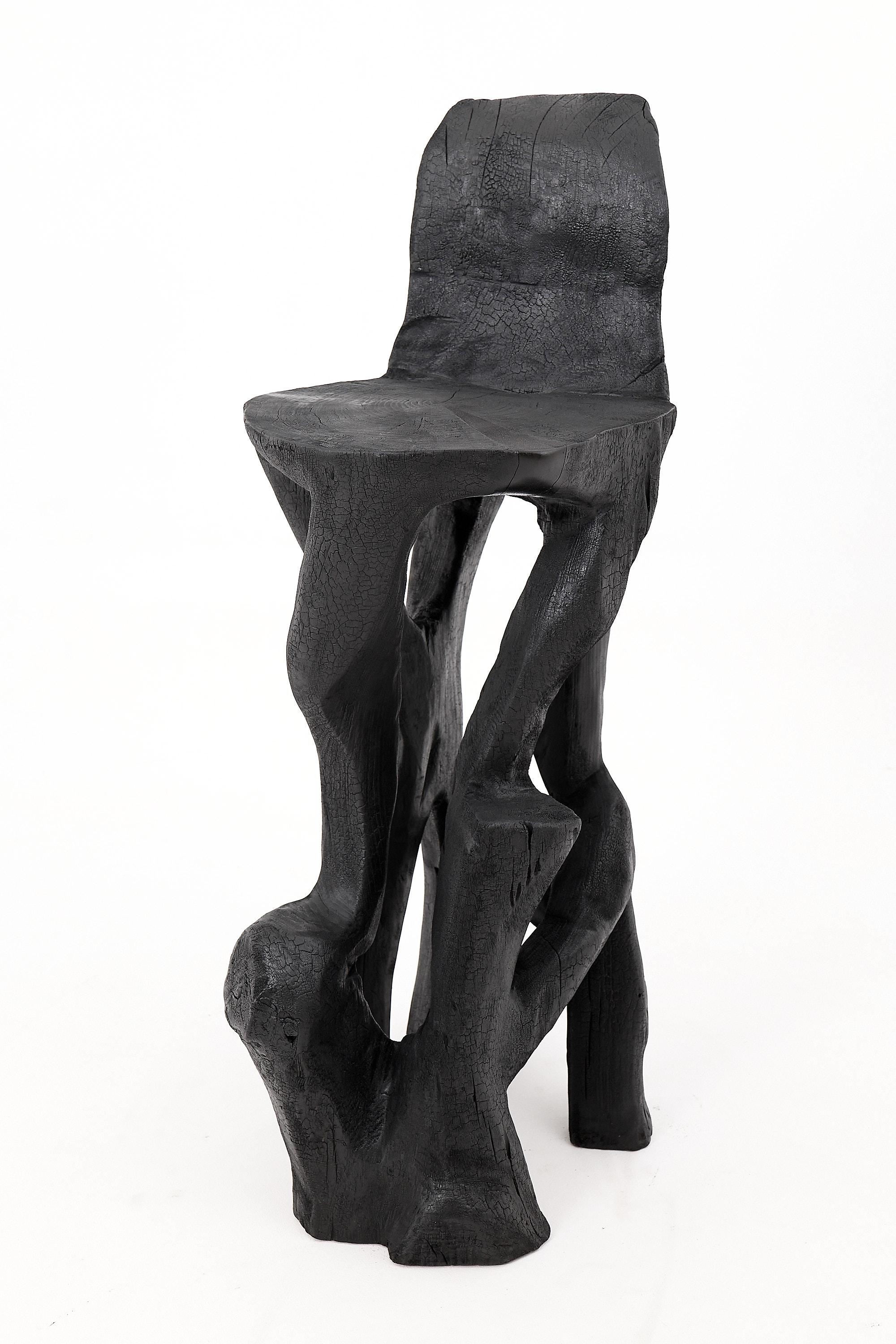 Esta silla escultural es una expresión singular de artesanía en bruto, tallada a mano a partir de un tronco macizo de madera dura y ennegrecida mediante la antigua técnica japonesa shou sugi ban. Su espectacular base en forma de raíz se eleva hacia