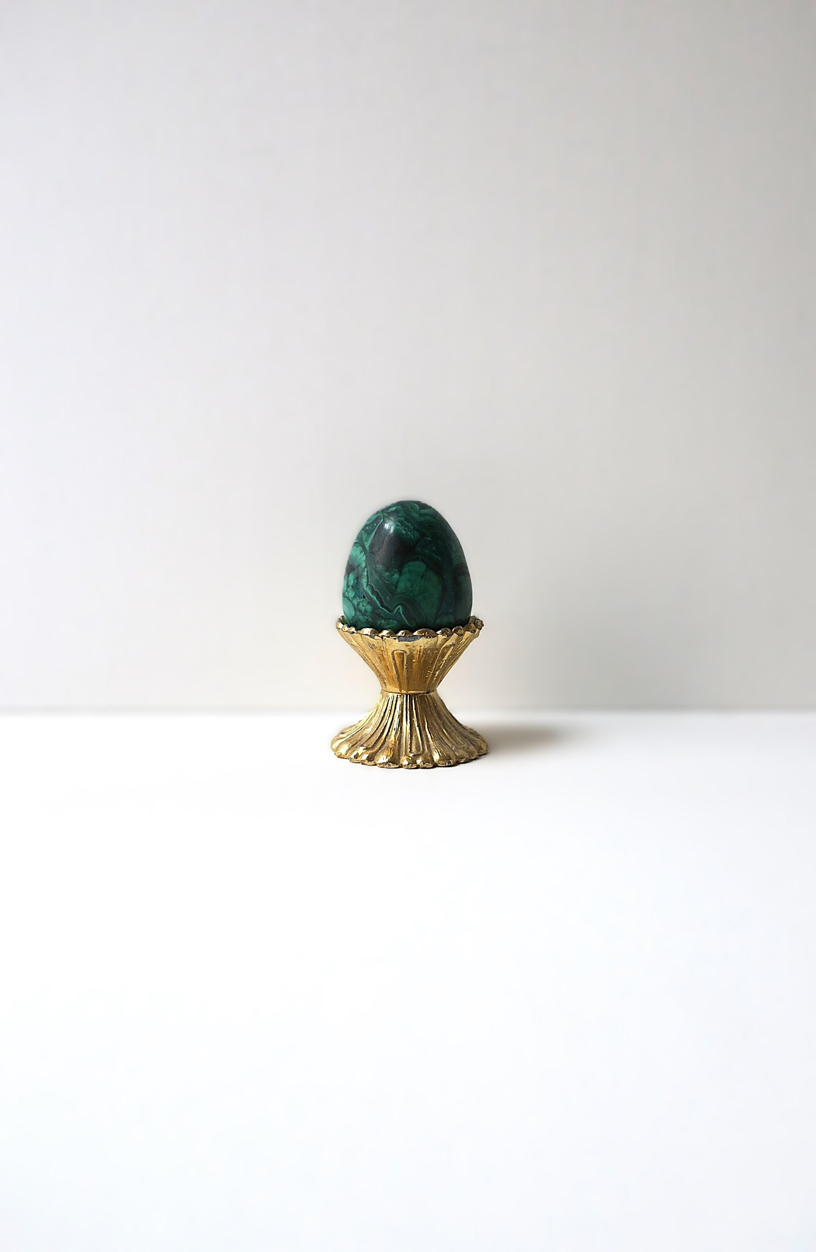 Precioso objeto decorativo escultura de huevo de malaquita verde sobre base acanalada de latón dorado, hacia mediados del siglo XX. El objeto huevo de malaquita tiene un bonito diseño/color, la pieza está hecha a mano, con una base estriada de latón