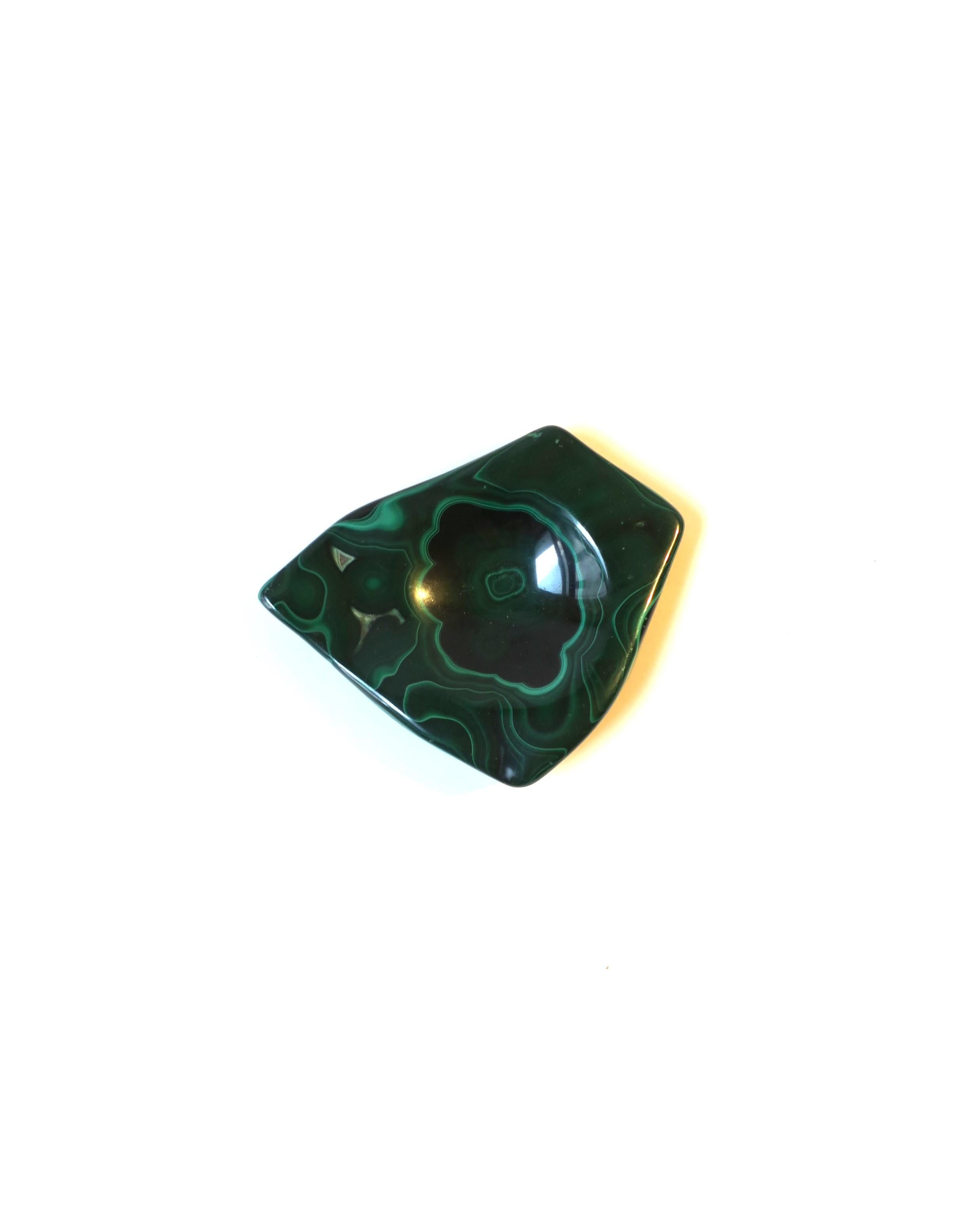 A beautiful natural emerald green malachite jewelry dish vide-poche with an abstract shape, in the organic modern style. A great piece for a desk, vanity, nightstand table, or other area to hold small items. Shown holding a cocktail ring. A