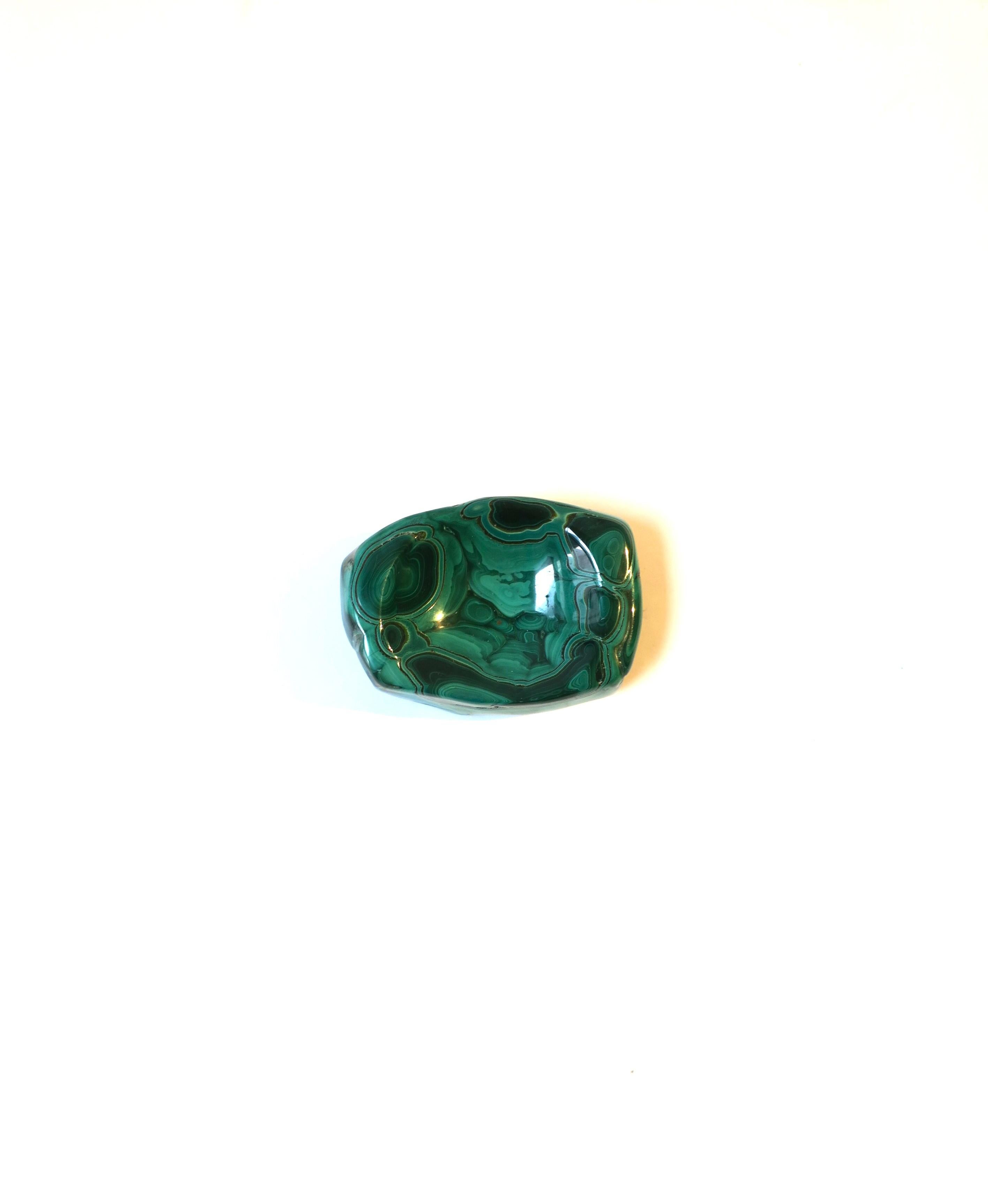 A beautiful natural emerald green malachite jewelry dish vide-poche, in the organic modern style. A great piece for a desk, vanity, nightstand table, or other area to hold small items. Shown holding earrings. A beautiful malachite vessel, polished
