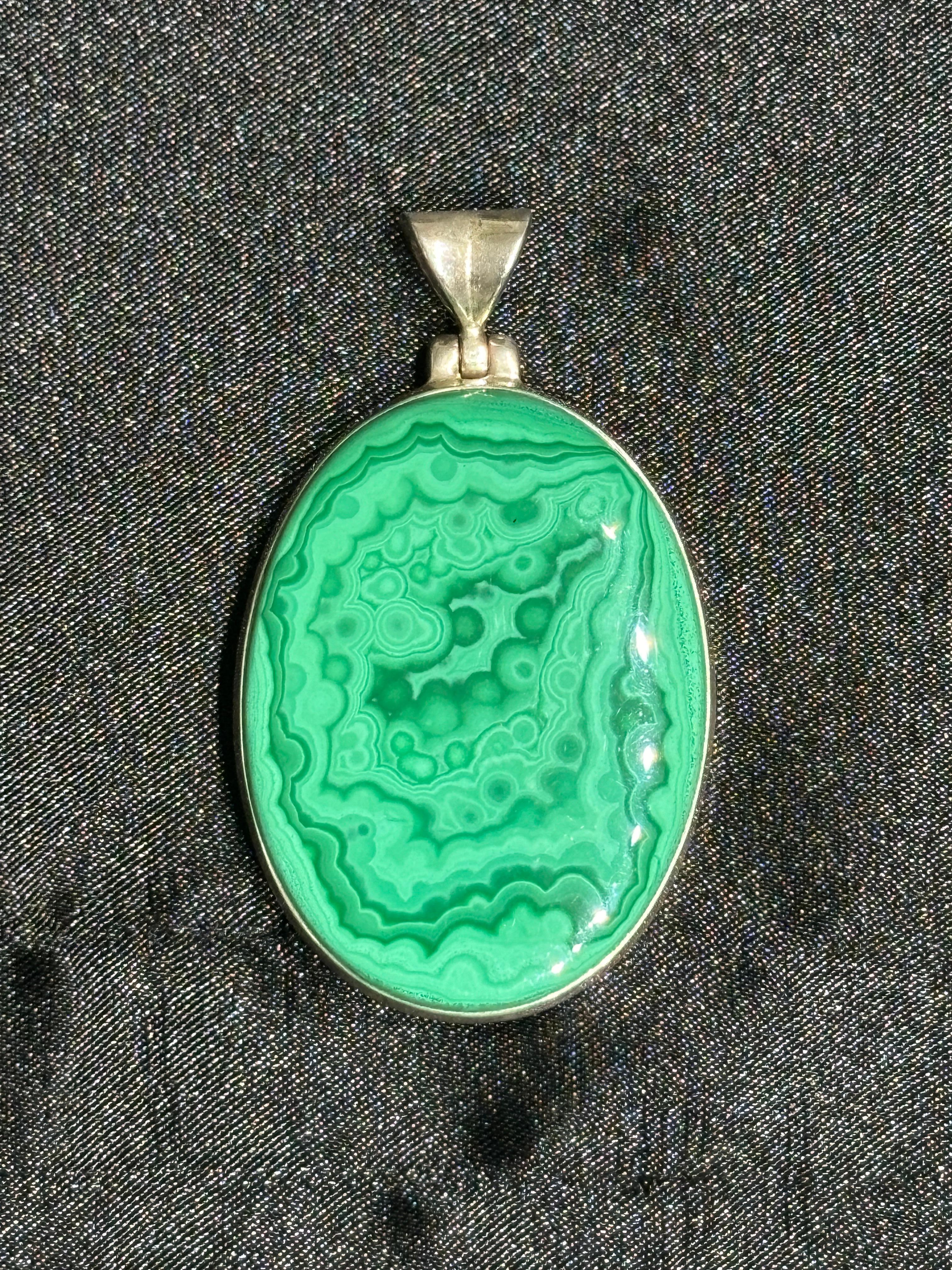 Ciondolo di malachite in argento Sterling realizzato a mano.

Questo raffinato ciondolo è caratterizzato da una vibrante pietra di malachite, nota per i suoi affascinanti motivi a bande nei toni del verde. Realizzata a mano in argento sterling 925,