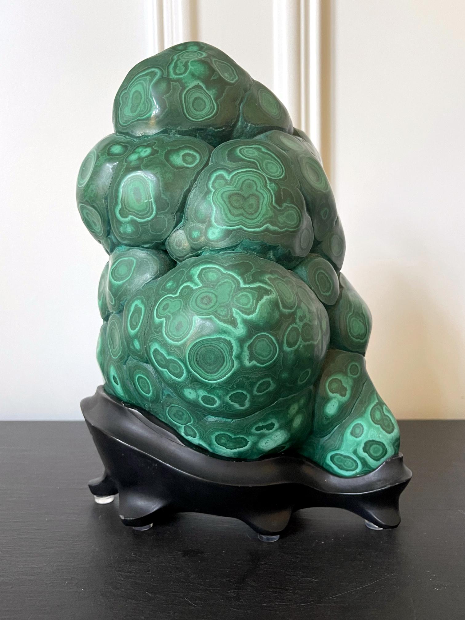 A malachite rock specimen with intense green and black colors fitted on a wood stand and displayed as a Chinese scholar stone. The gemstone in the botryoidal form was polished in all sides except the back with a natural fissure to reveal the