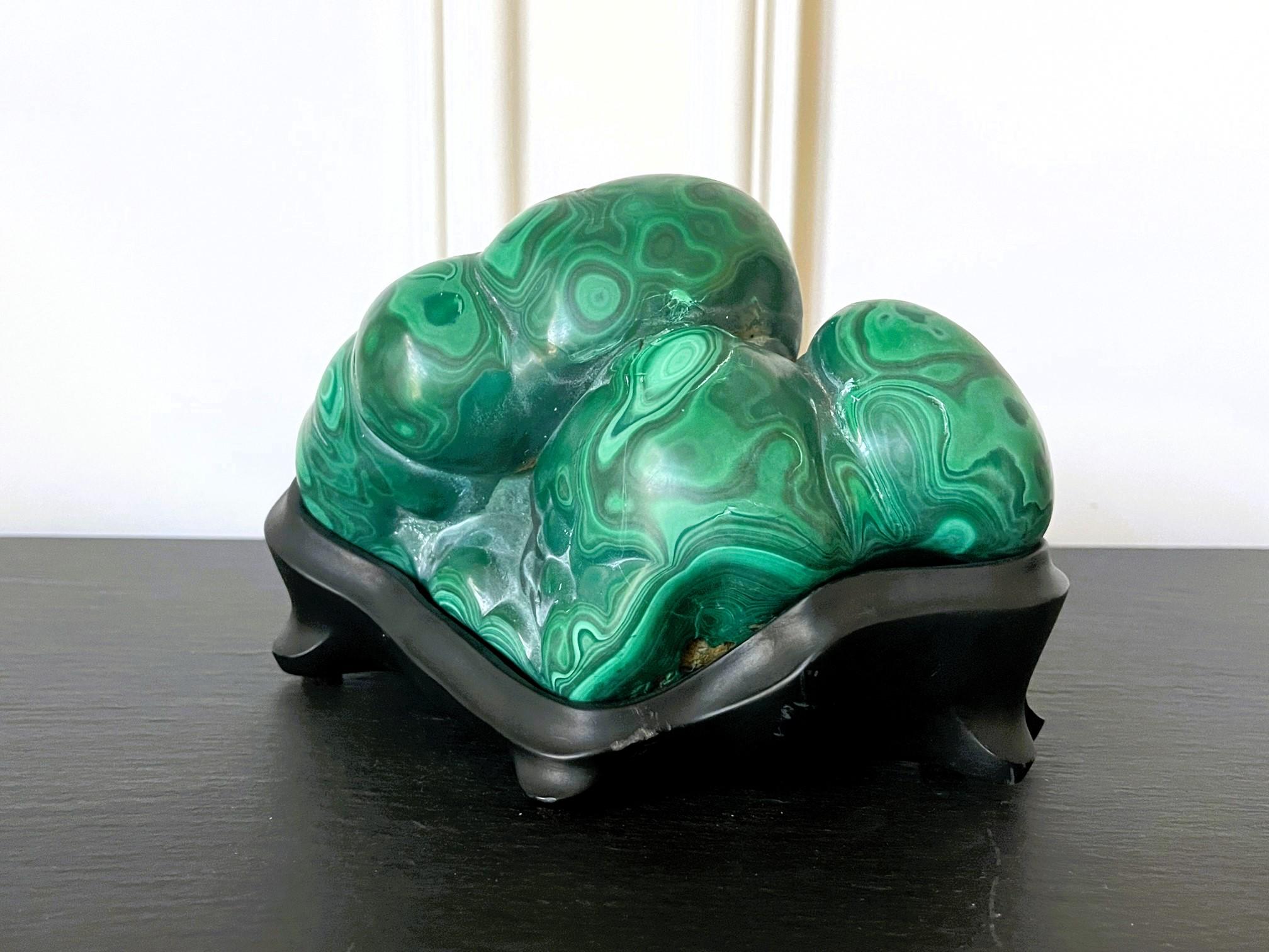 Displayed on a black custom carved wood stand, this solid malachite rock specimen with intense green and black colors functions as a Chinese scholar stone. The gemstone showcases the prominent botryoidal form and was polished on all sides revealing