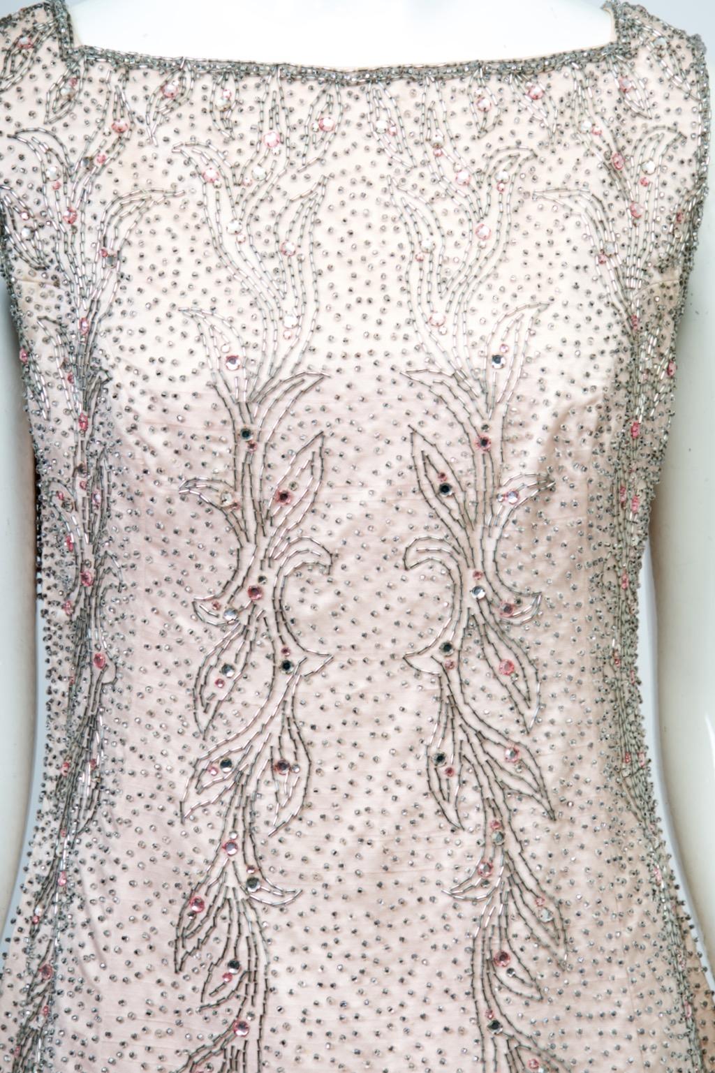 1960s evening dress by Malcolm Starr in pale pink satin with beaded emellishment throughout. This consists of primarily silver beads in various shapes and sizes, the body covered with tiny seed beads, while cascading leaf-form motifs in silver bugle