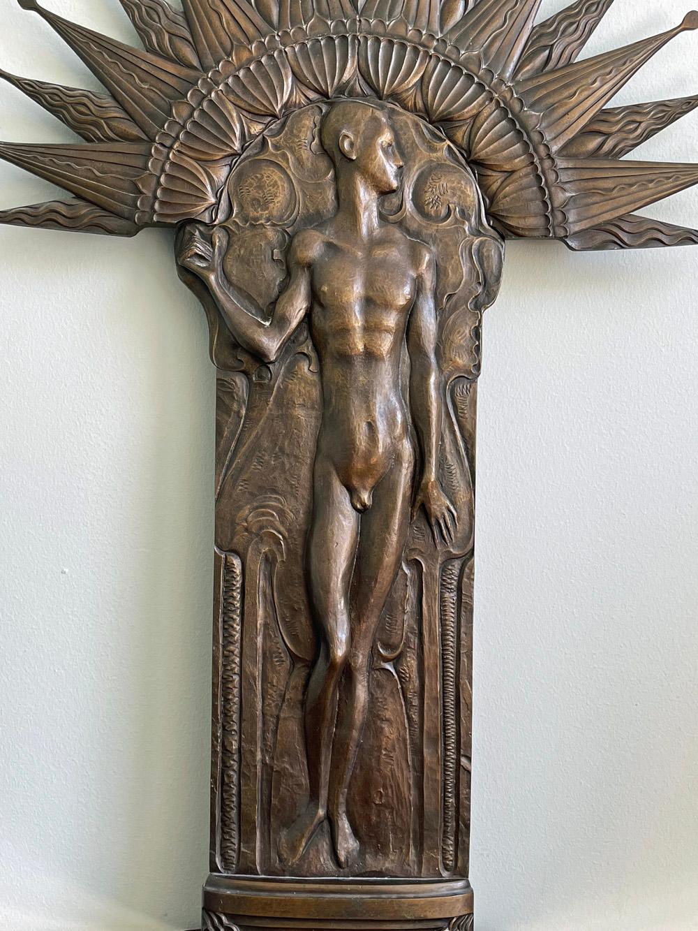 Grande et spectaculaire, cette sculpture en bronze en relief représente un nu masculin debout sur un sol riche en motifs décoratifs courbes - comme si l'atmosphère était vivante - surmonté d'une auréole audacieuse et rayonnante. Conçue pour être
