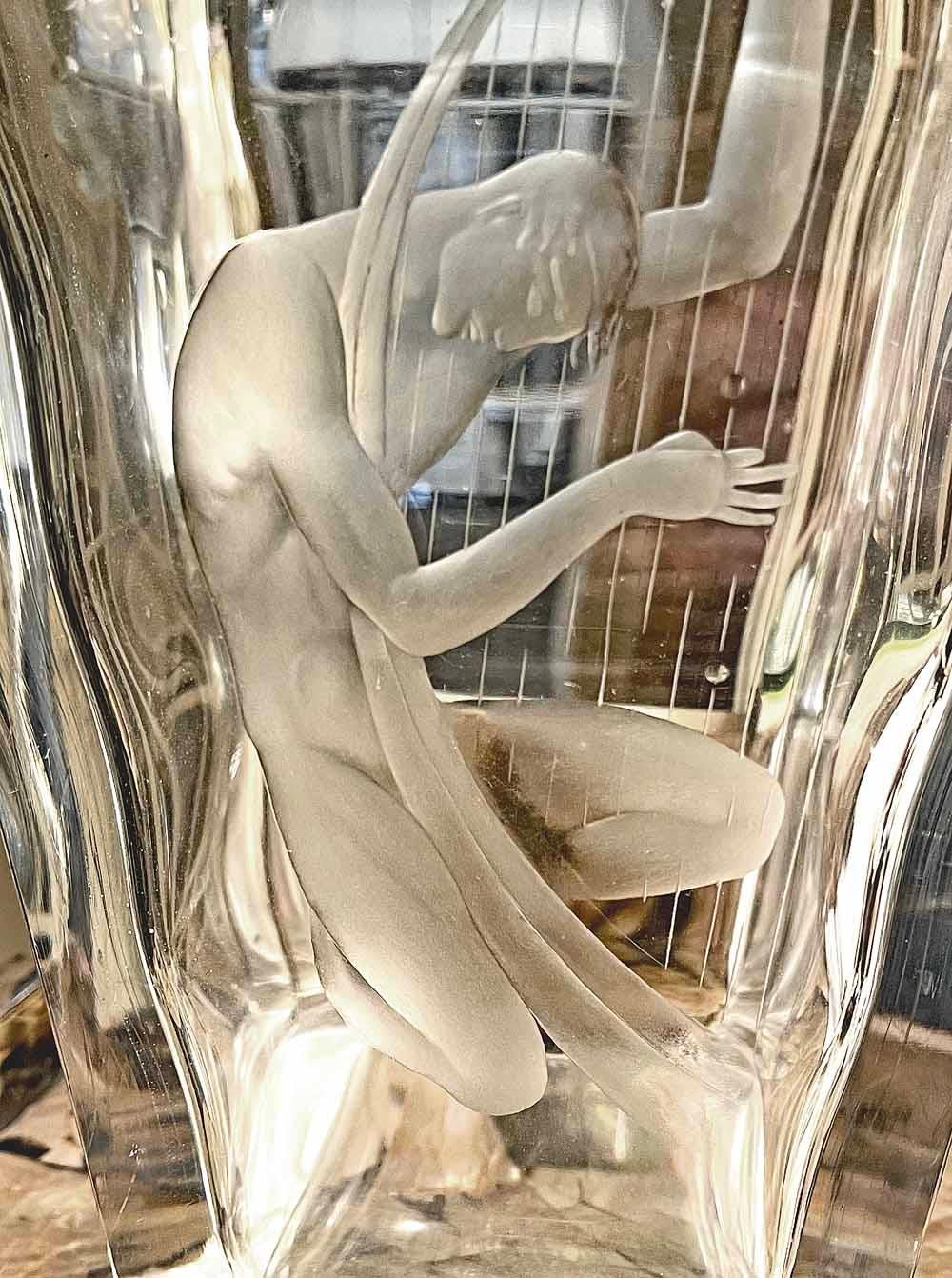 Cette pièce, l'une des figures nues stylisées et élégantes de Vicke Lindstrand pour la verrerie Orrefors en Suède à l'apogée de l'ère Art déco en 1939, présente une figure masculine gravée jouant d'une harpe de la taille d'une vie, décorant un vase