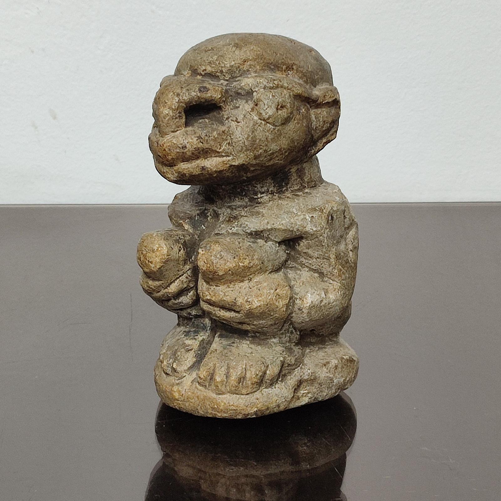 A Kisii Nomoli carved stone figure, a male with his hands wrapped around his knees, on a base; from the Kissi people of Sierra Leone.
Greyish brown patina, snout-like mouth, large nose, slight traces of abrasion.
Such figures were used in