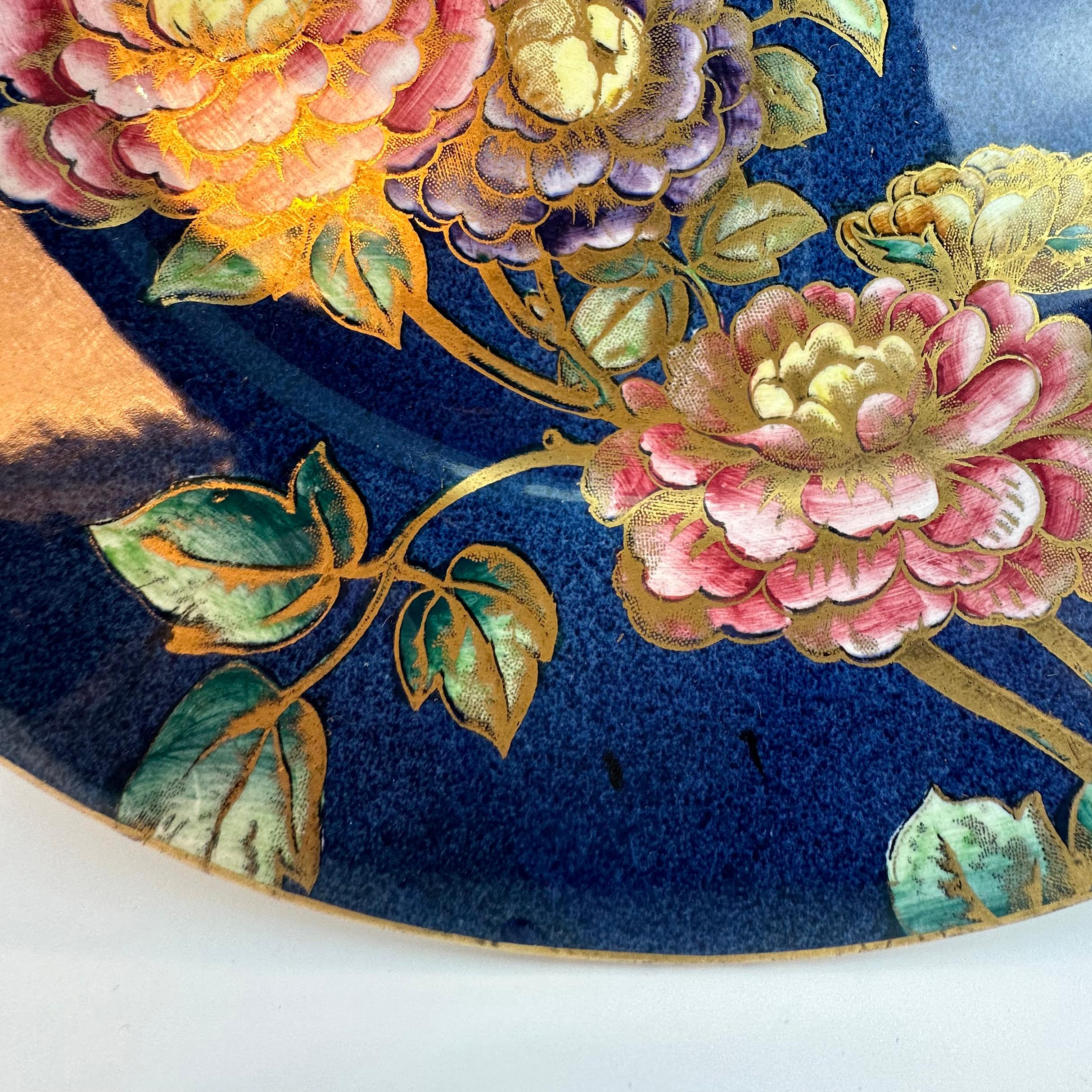 An exquisite porcelain wall plaque, crafted by the renowned Newcastle pottery company, Maling.

The large wall plaque boasts a rich, deep mottled azure blue base, providing a striking backdrop for a delicate floral illustration of climbing roses.