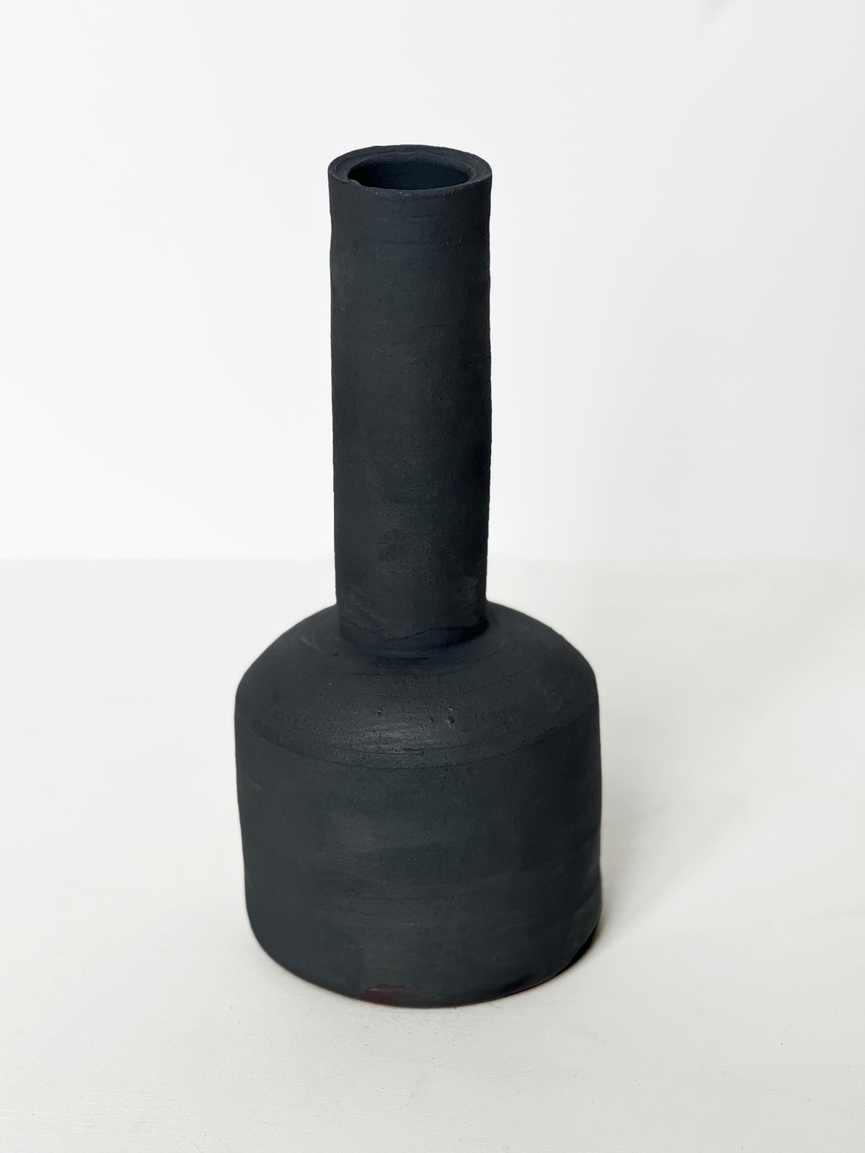 Handgefertigtes und sorgfältig verarbeitetes Stück aus Steingut in dunkelgrau/schwarzer Farbe.  Diese Vase hat einen breiteren runden Boden und einen langen Hals.  Mit ihrer matten Oberfläche und der weichen Haptik eignet sich diese Vase perfekt zur