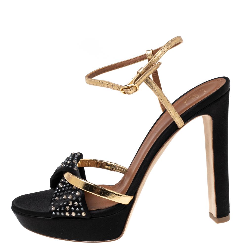 Malone Souliers offers the perfect blend of luxury and style with these platform sandals. The fabulous upper of these sandals show black satin and gold leather with embellishments on the frontal strap. Block heels measuring 12 cm are incorporated