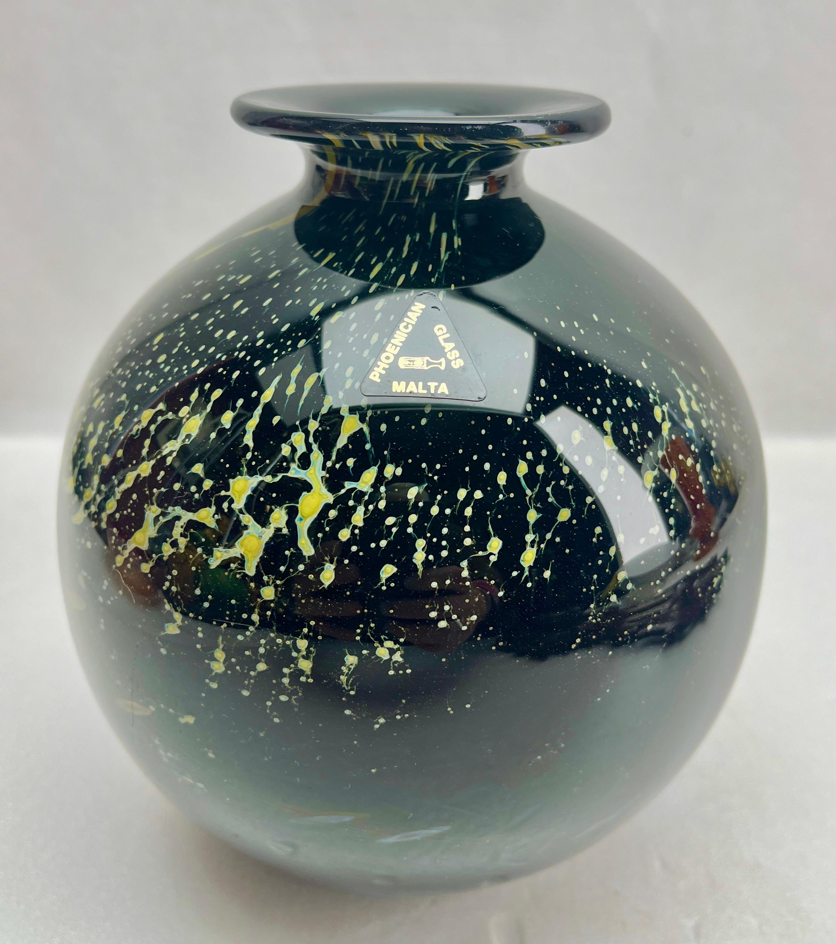 Jarrón solifleur de Malta soplado a mano con la boca de borde ancho, (1970-1975).
Presenta colores típicamente mediterráneos, hilos de color verde marino arremolinados sobre una base de vidrio amarillo verdoso con inclusiones de burbujas.
Fabricado