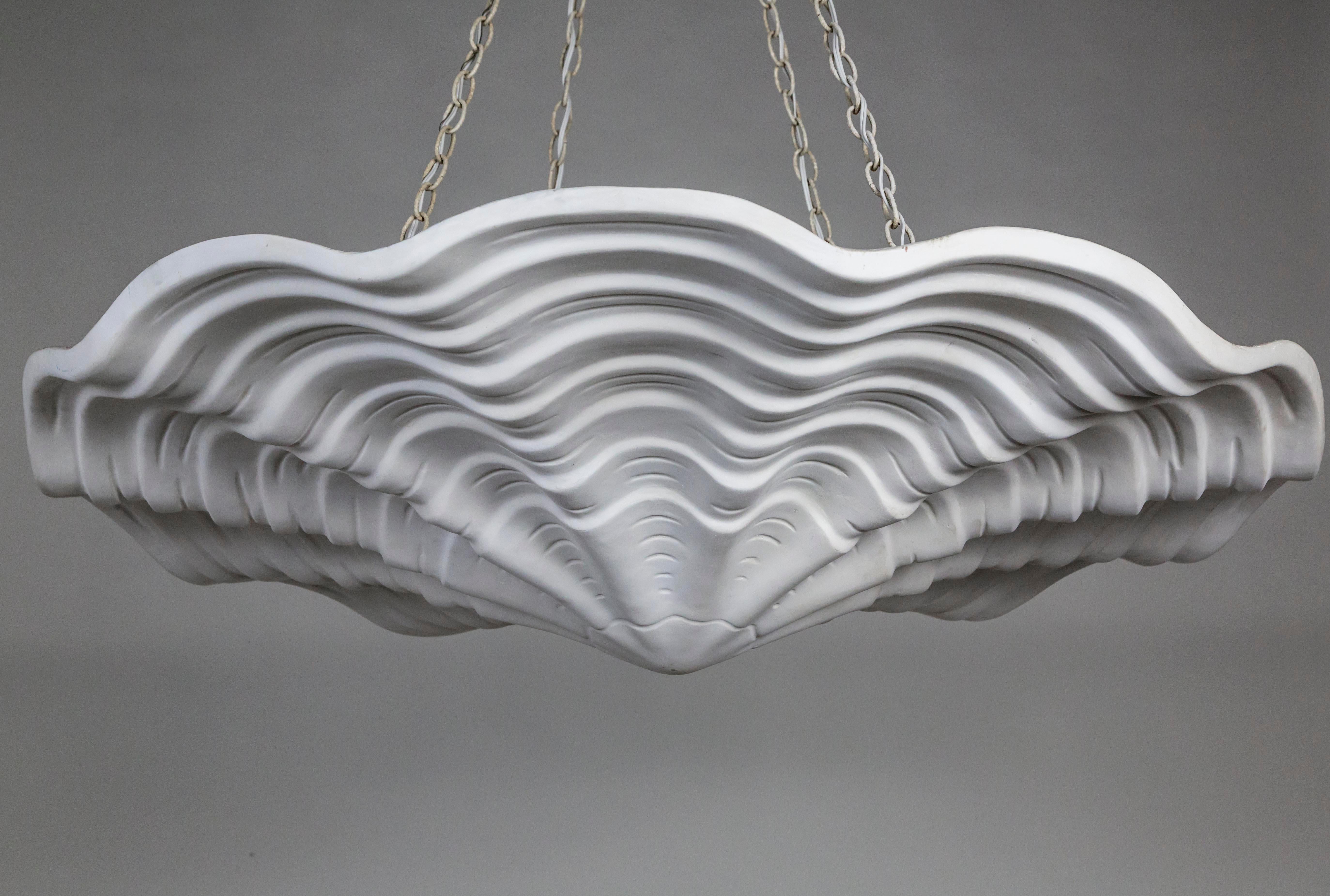 A lacquered plaster pendant in an undulating shell shape, with scalloped edges and imprinted lines accentuating the form. A newer take on Francis Elkins's 1940s plaster plafonnier. Hanging by four chains; with 4 medium base ceramic sockets.