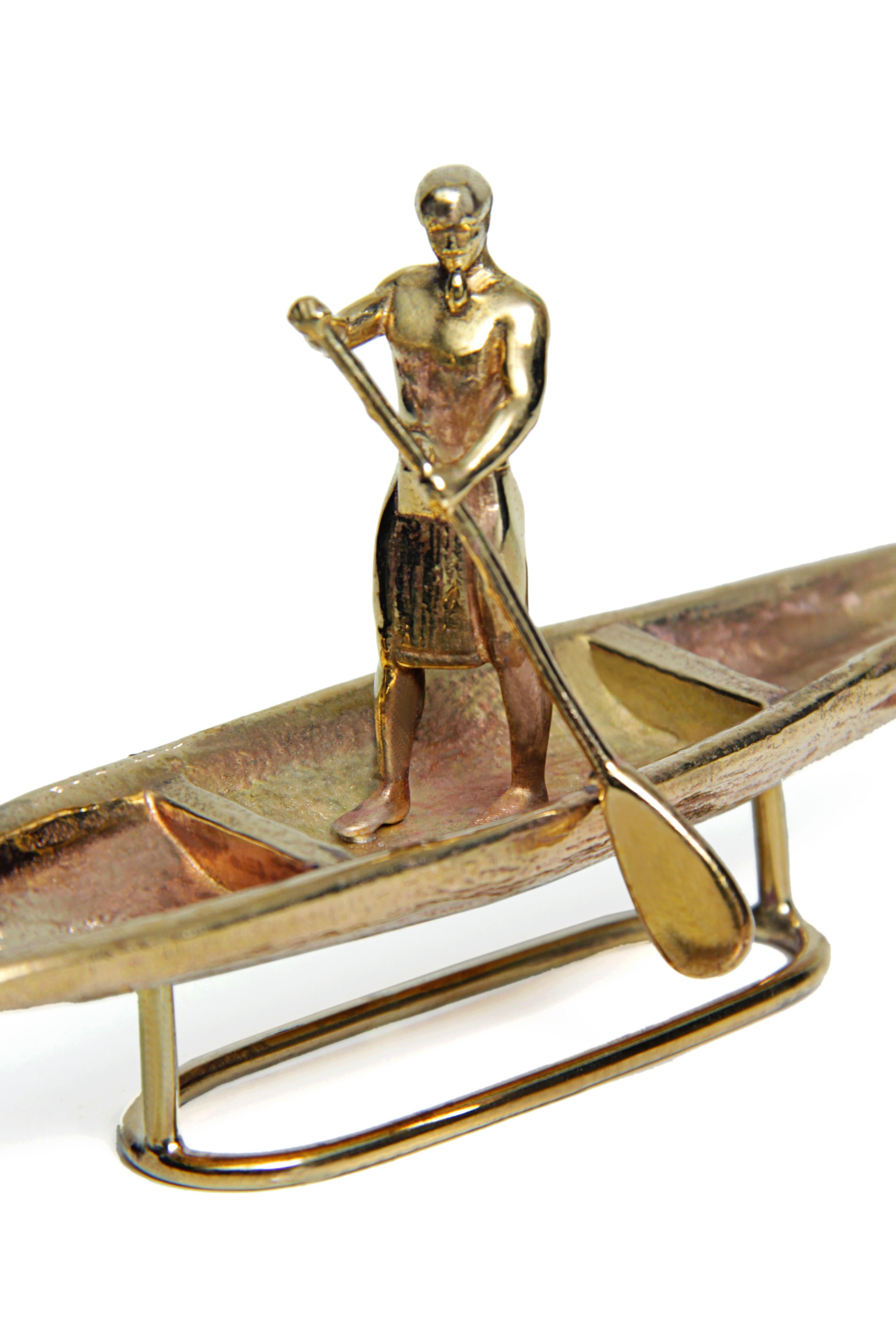 This polished brass sculpture of a man in a wooden canoe is a representation of the peaceful and timeless experience of living by the Amazon River, coming and going. Placing him on any surface will turn it into a stream of river where you can just