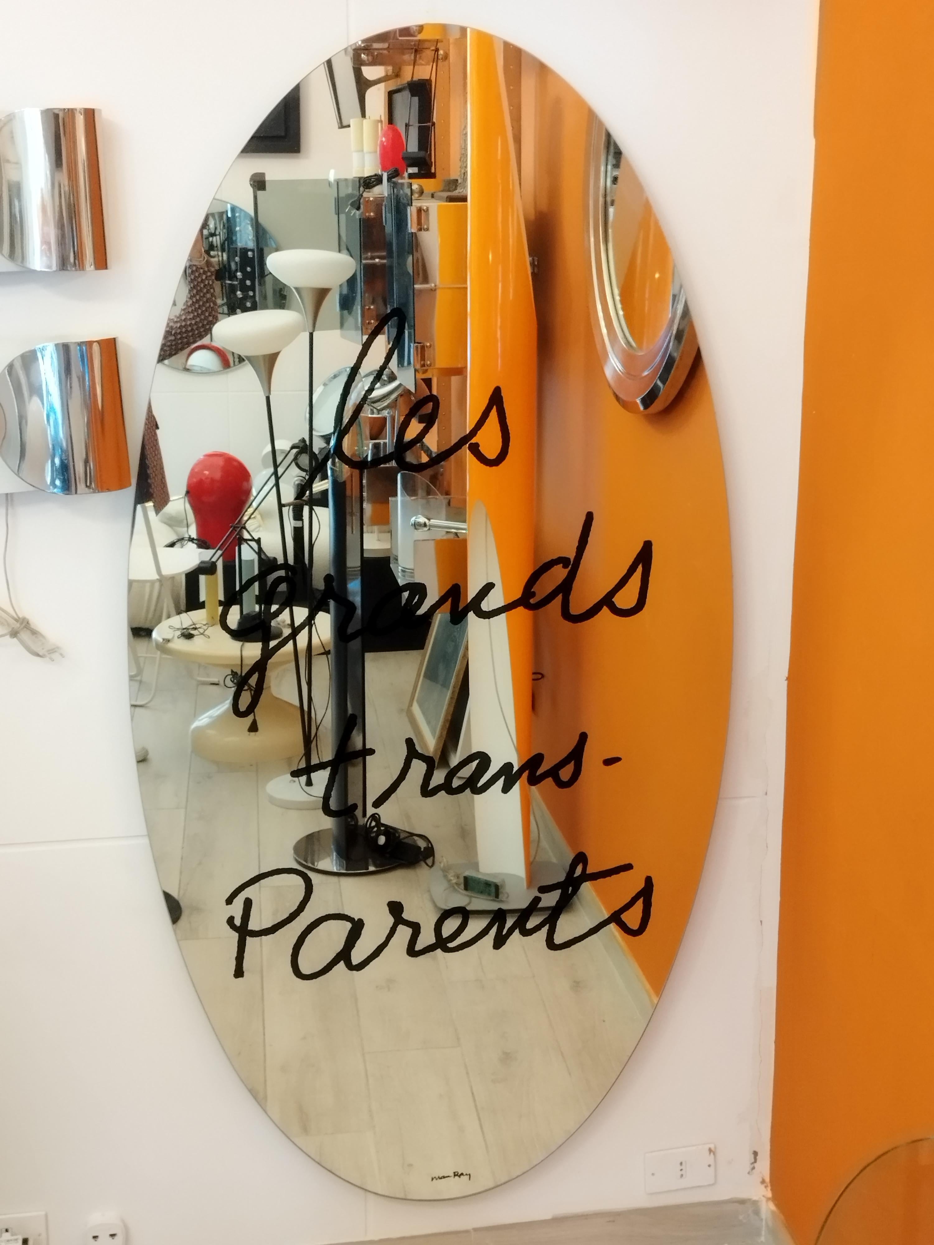 Designed in 1938 by Man Ray. This elliptical mirror is serigraphed with “les grands trans-Parents.” A play on words written by Man Ray on a mirror, a poetical proposal for the home. This mirror was originally made for Simon Gavina in 1971 and is