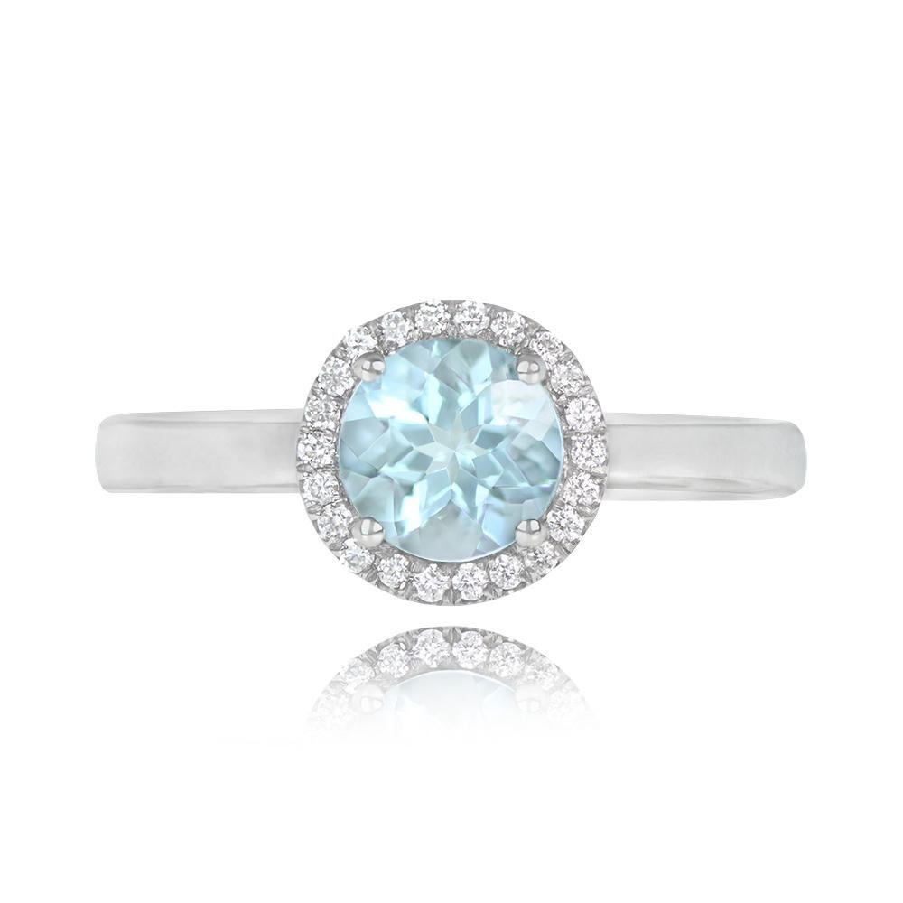 A stunning white gold ring with a lively round-cut aquamarine weighing around 0.80 carats, surrounded by a row of round full-cut diamonds. The ring showcases an open-work under-gallery.

Ring Size: 6.5 US, Resizable
Signed: Manda
Metal: Gold, White
