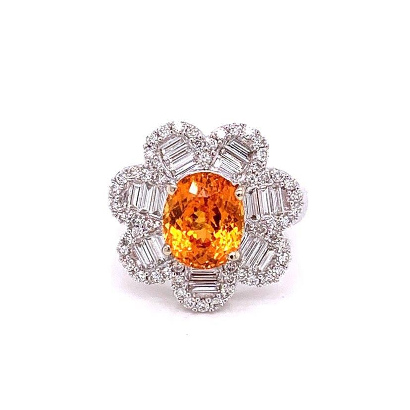 A special ring designed as a flower centered by a vivid orange mandarin garnet. It has a clean and clear crystal and weights 3.75 carats as a oval shape. It is accented by 1.08 carats of round and baguette cut diamonds all set in 18k white gold. A