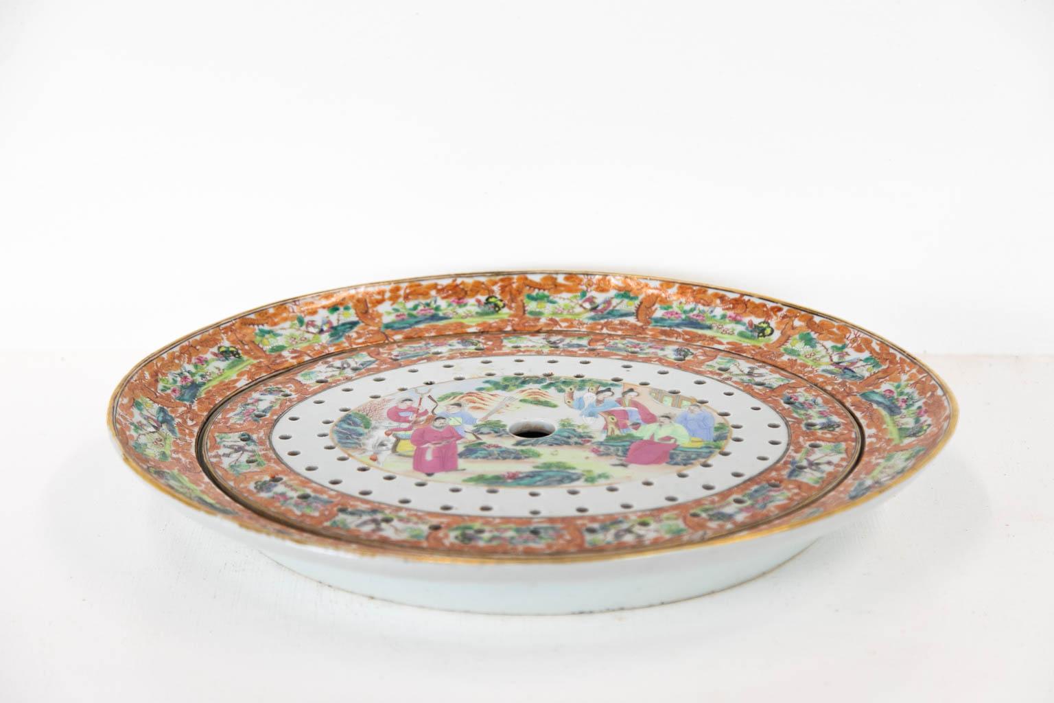 The center panel in both the platter and strainer have richly painted Mandarin court scenes which are framed with depiction of birds, butterflies, and flowers framed with stylized dragons. The strainer has a 1/2 by 1/4 inch chip on the bottom edge.