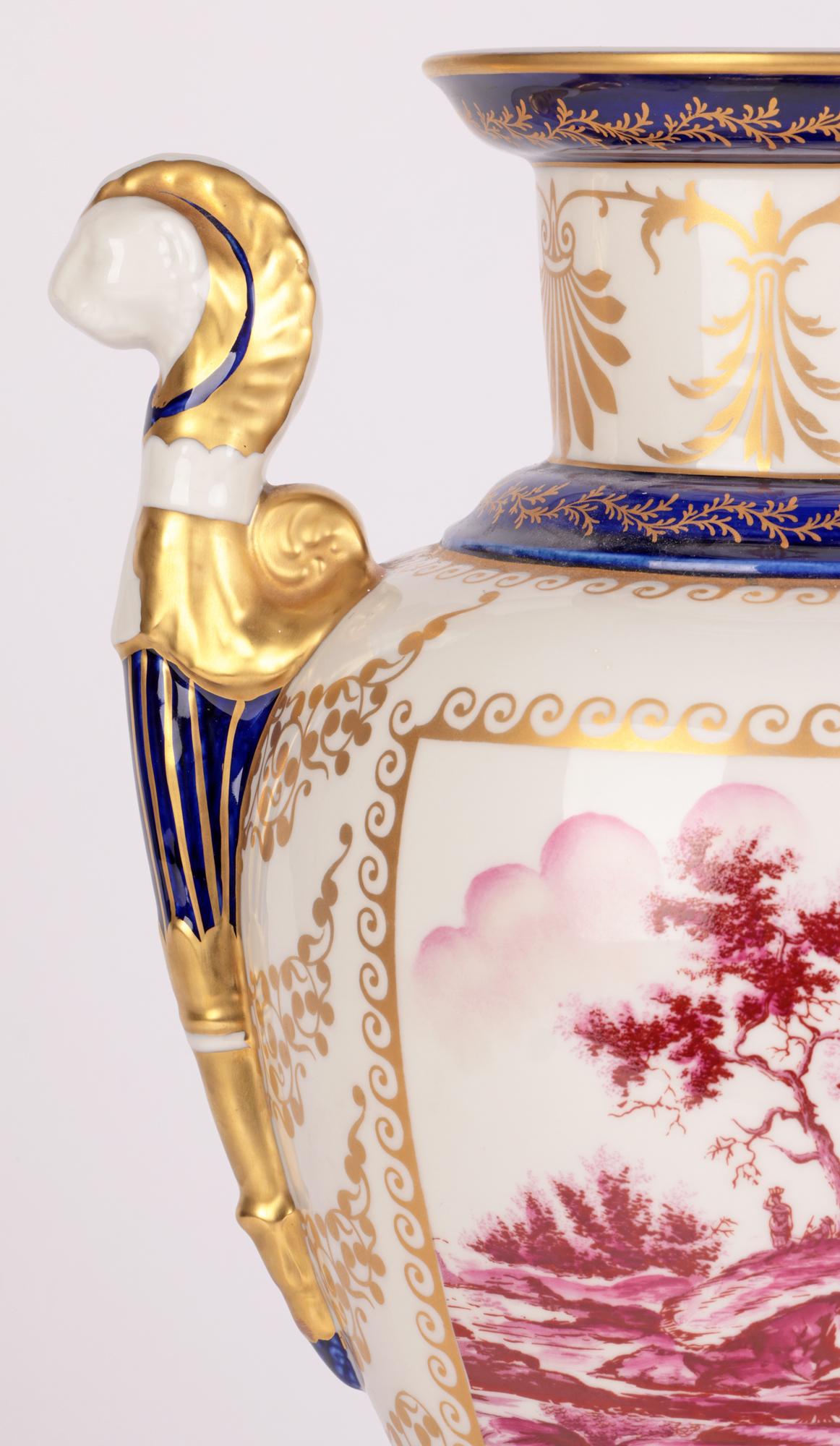 A large and stylish Italian porcelain twin handled pedestal vase hand painted with landscape scenes by Mangani and dating from the 20th century. This tall and elegant vase stands raised on a square shape pedestal base with an urn shaped body and