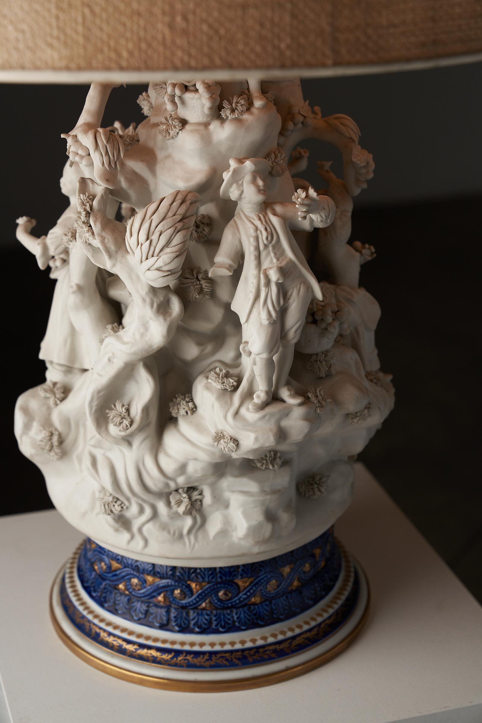This exquisite table lamp is a remarkable piece crafted by Mangani in the 1980s in Italy. The lamp features a detailed ceramic sculpture with intricate high relief forms of biscuit porcelain figures, set upon a beautifully decorated cobalt blue base