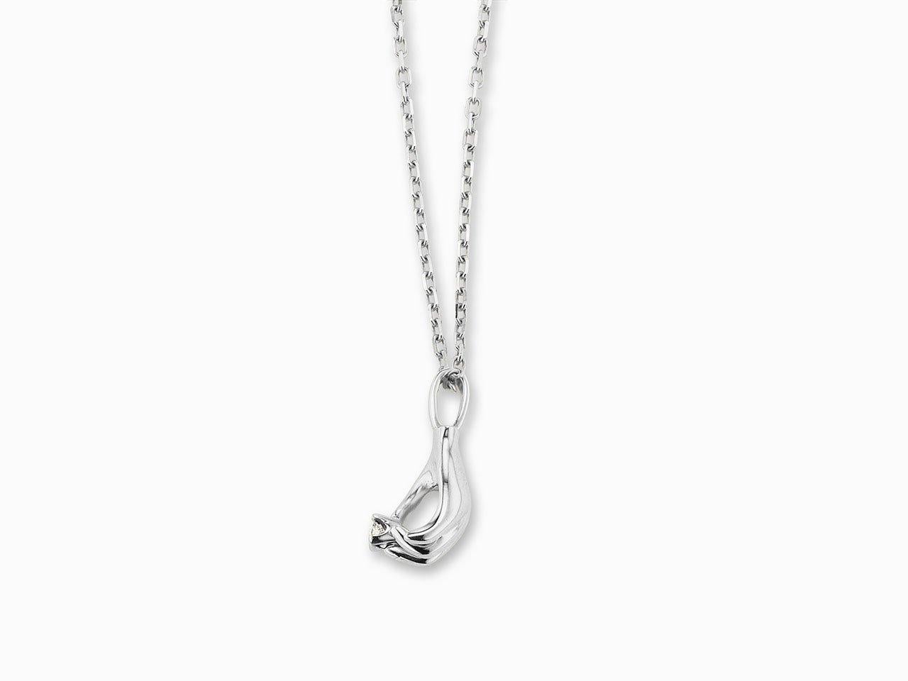 MANIAMANIA 'La Magicienne'  necklace in 14k White Gold, with hand motif pendant (22mm) holding a 3mm white diamond (0.1ct), on 14k white gold elongated cable chain (20 inch long).

A graceful hand charm pendant shows off a fiery white diamond in