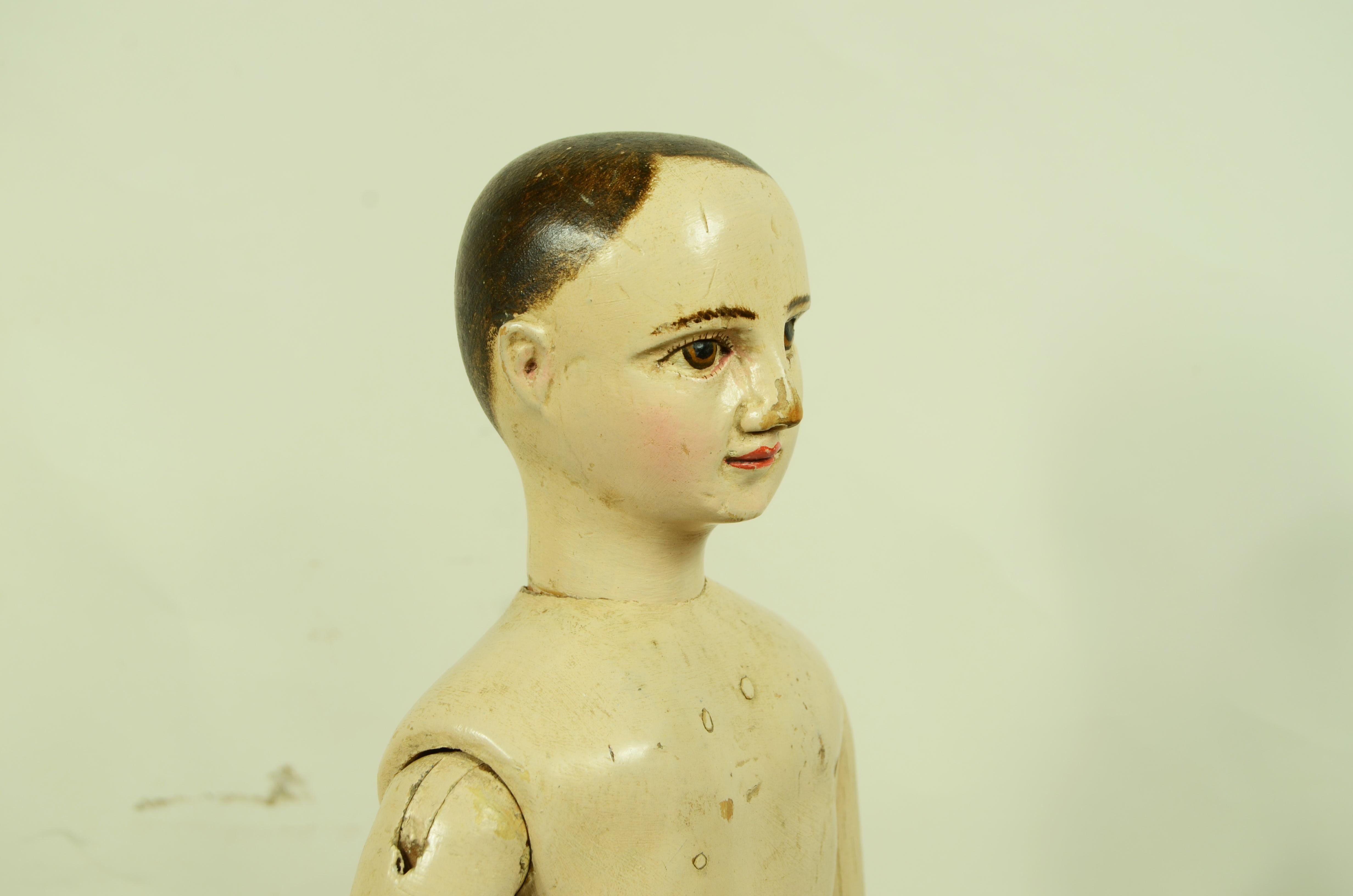 Manichino da artista in legno di faggio laccato color cipria raffigurante un giovane ragazzo dal viso espressivo con i capelli bruni corti, gli occhi con ciglia e sopracciglia  brune e la bocca dalle labbra tinte di rosso. 
Completamente snodabile