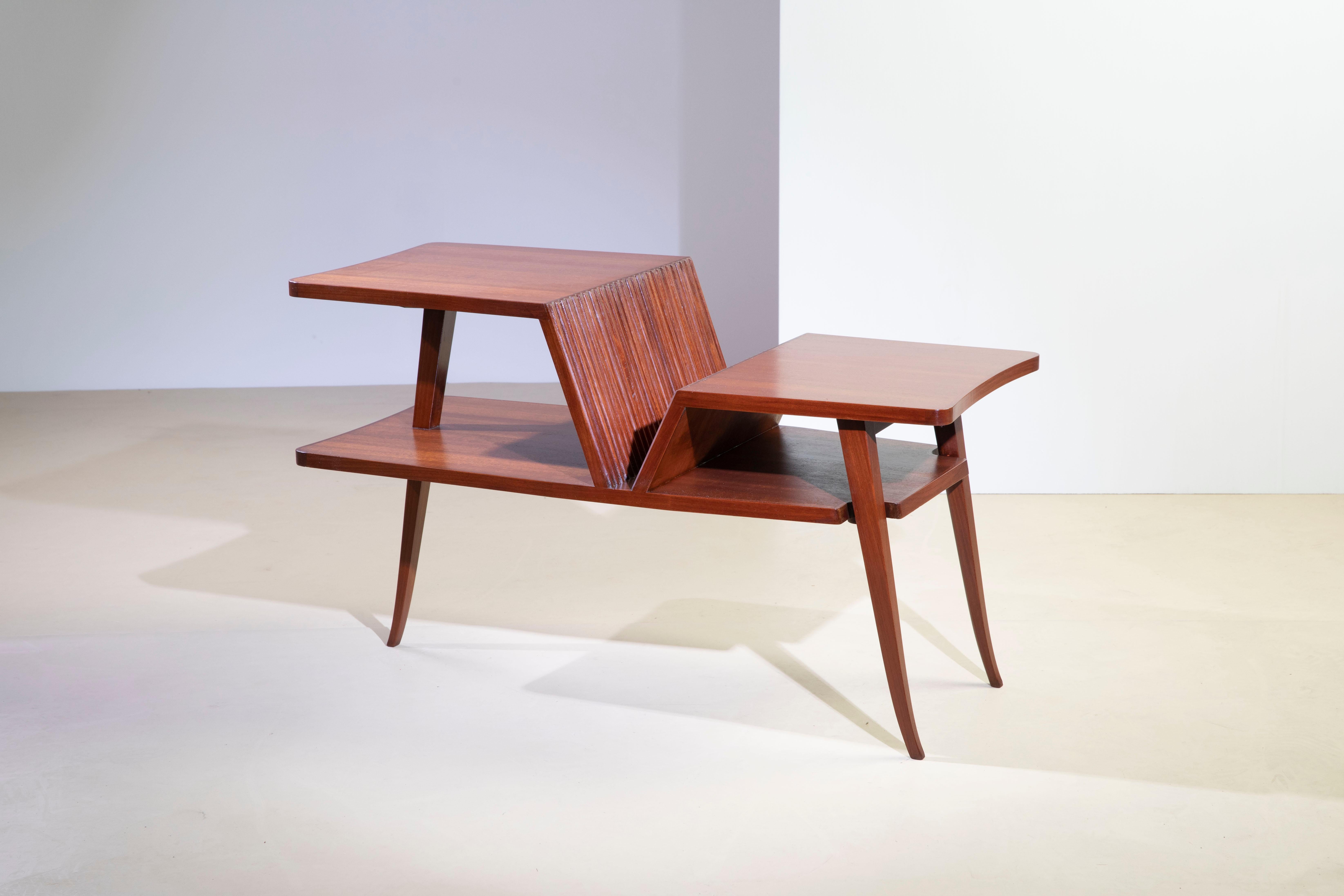 Polished wood coffee table in mahogany colors, 1950s, Italian made. It features a binding combination in the forms, supported by three legs and a distinctive and peculiar grissin on the sloping top.