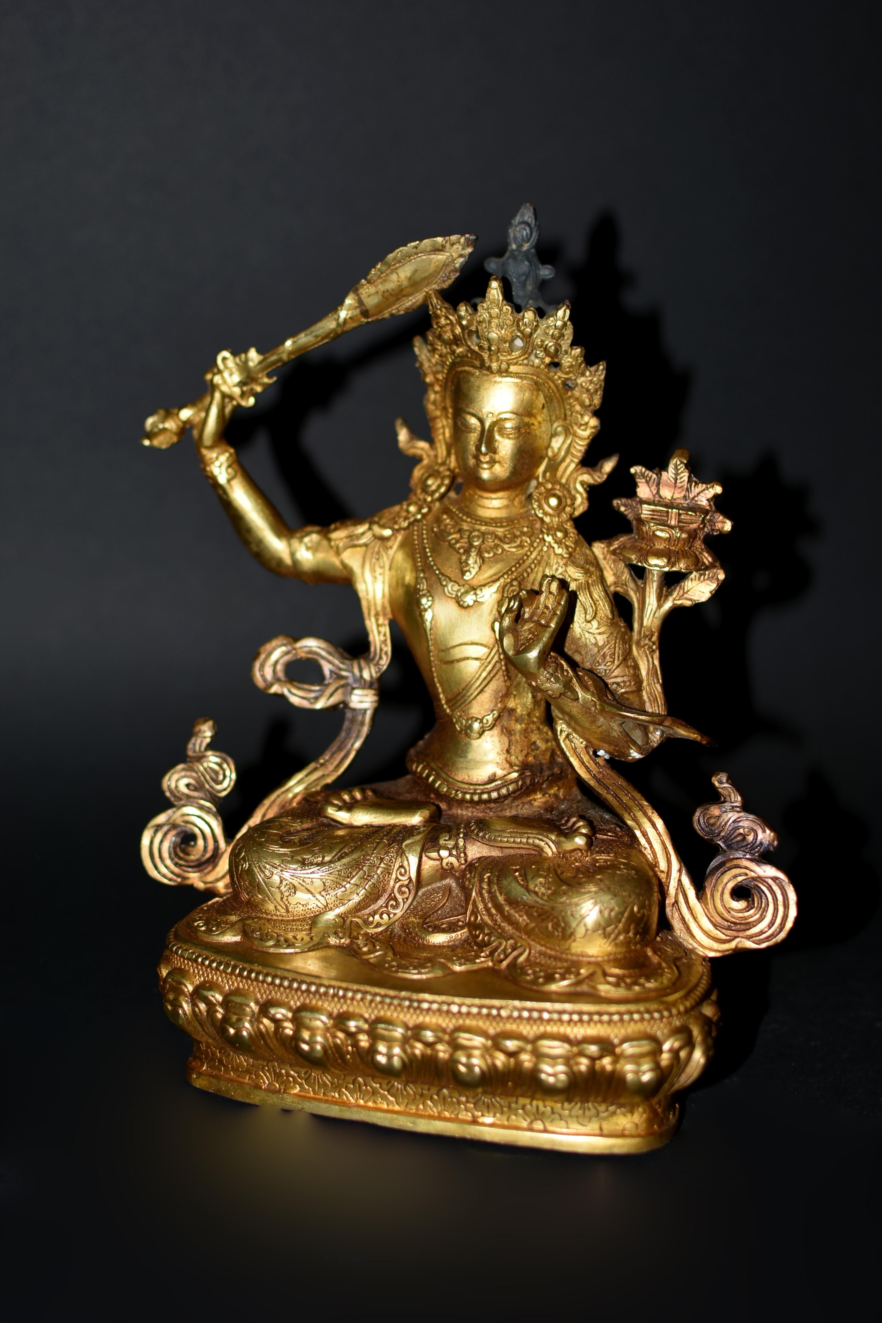 A beautiful gilt bronze statue of Tibetan Bodhisattva Manjushree. Seated in vajrasana on double lotus base, his right hand holding the sword of wisdom and his left hand holding the stem of a lotus in jnana mudra, gesture of teaching. The serene face