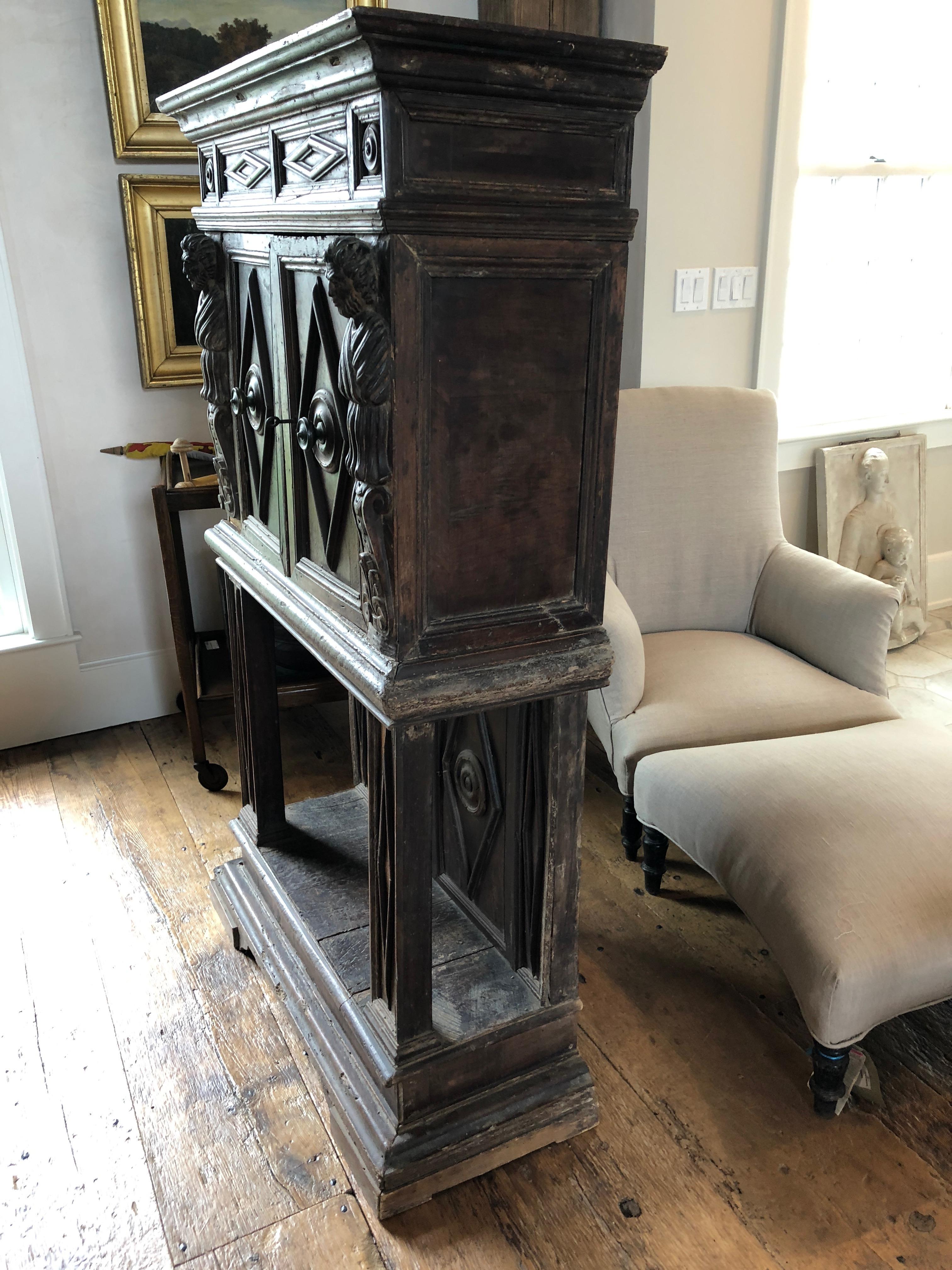 Two-part walnut cabinet on stand, with figural stiles of beautifully carved men with palm leaves below, carved and molded cornice, two diamond molded panel doors with dental original knobs, over three shelves, on a panel-back stand with molded front