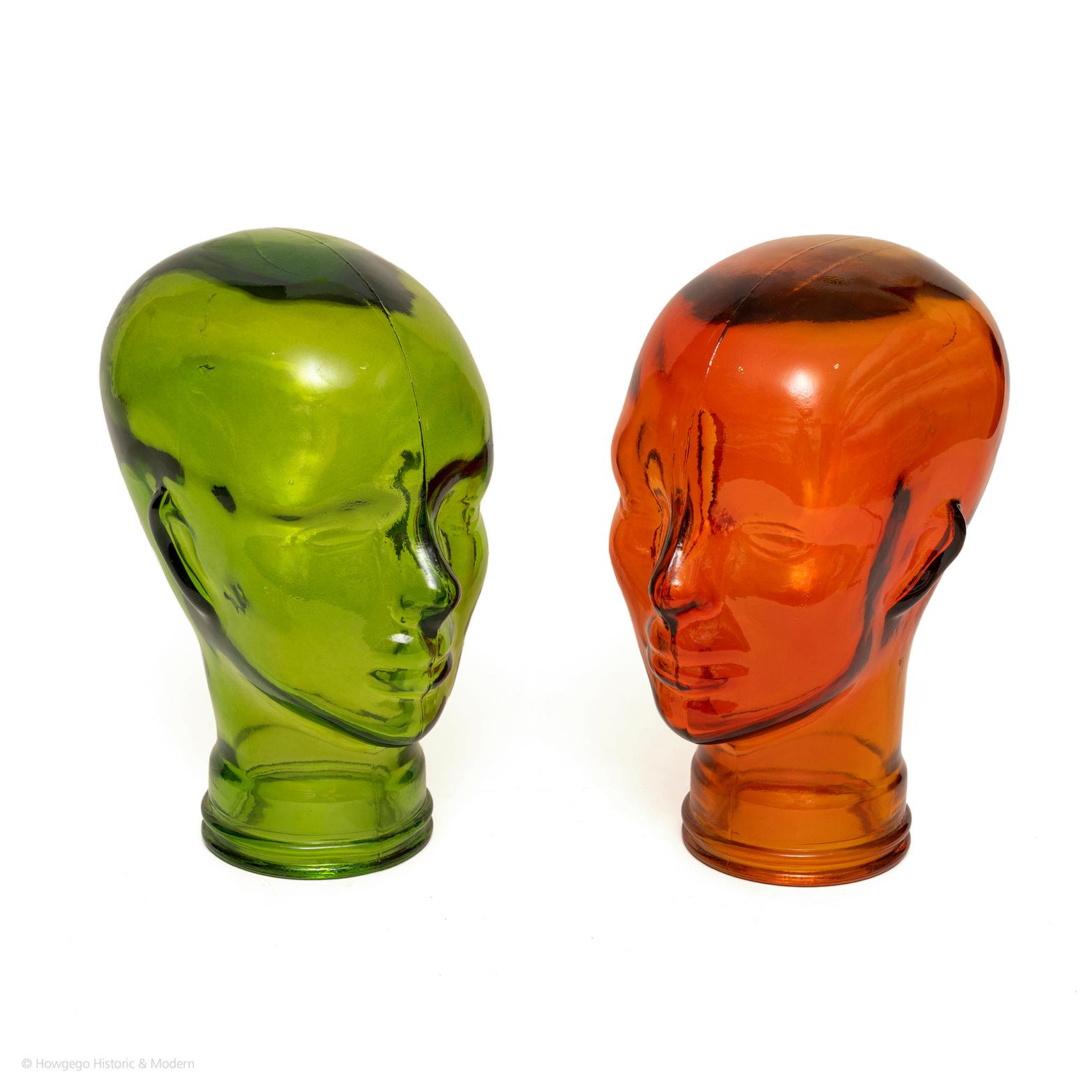 A pair of funky, vintage, coloured glass mannequin heads: one green, the other orange.  Designed for shop displays of hats, wigs, glasses etc and sometimes attached to full-body mannequins. 

Perfect conversation piece for displaying and storing