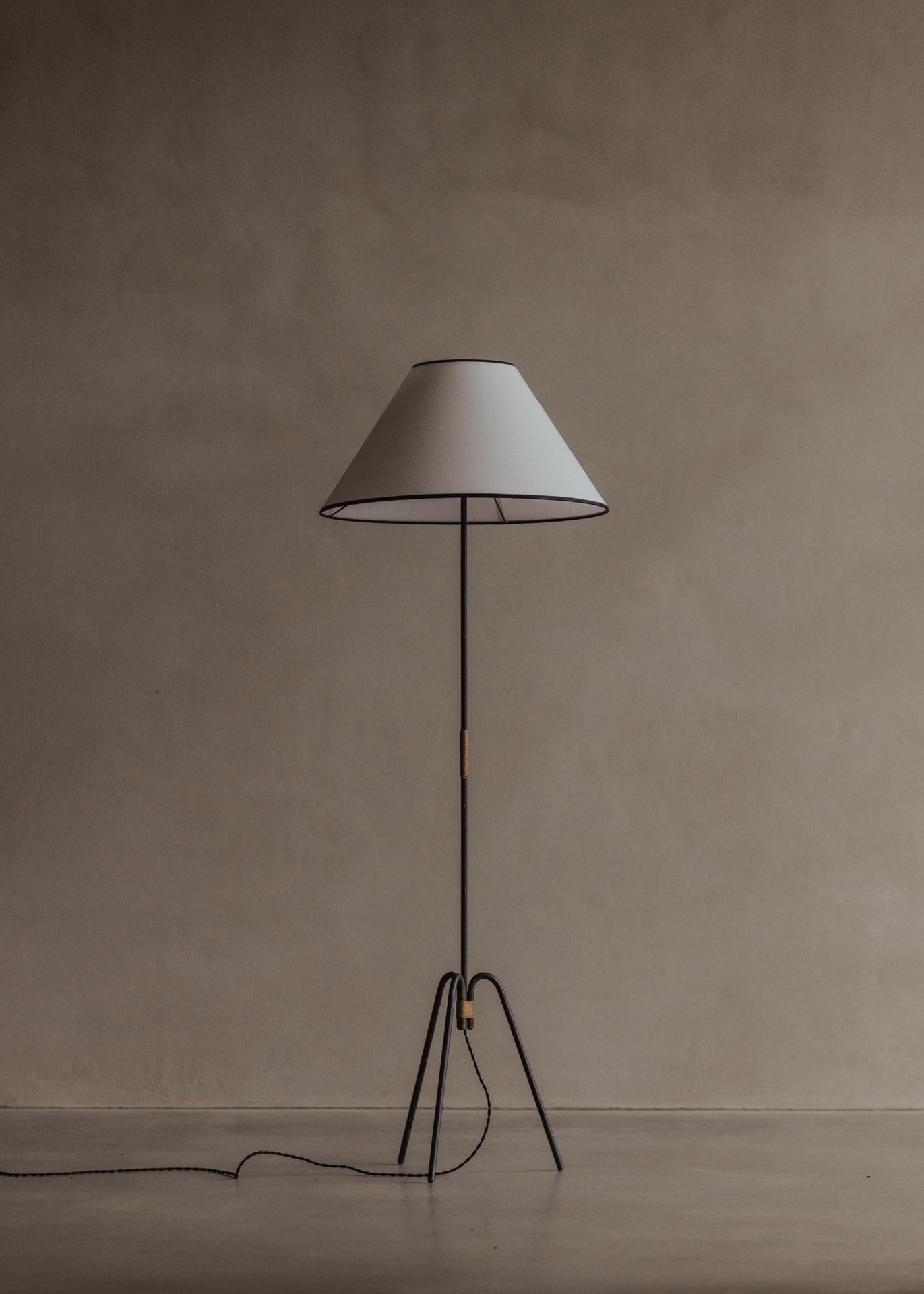 Beautiful wrought iron lamp with a tripod base, reminiscent of the work of Royère. The rattan details are sometimes found in the work of Jacques Adnet. The lamp is of French origin, estimated to be mid-20th century. It has been rewired and fitted