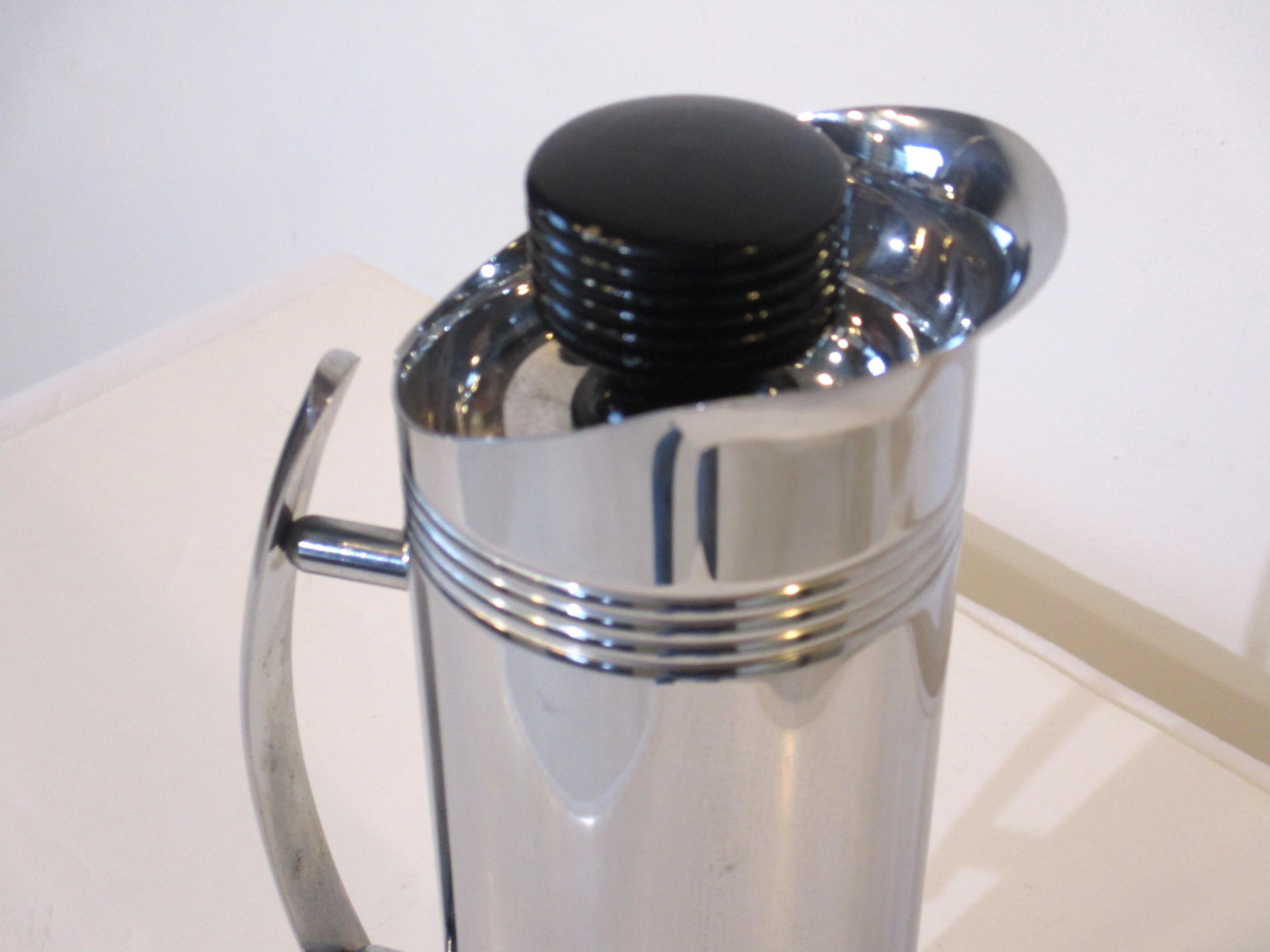 A very stylish chrome cocktail shaker and hot or cold pitcher with curved handle and black ribbed stopper having a cork end . In the manner of Art deco manufactured by the Manning Bowman company.