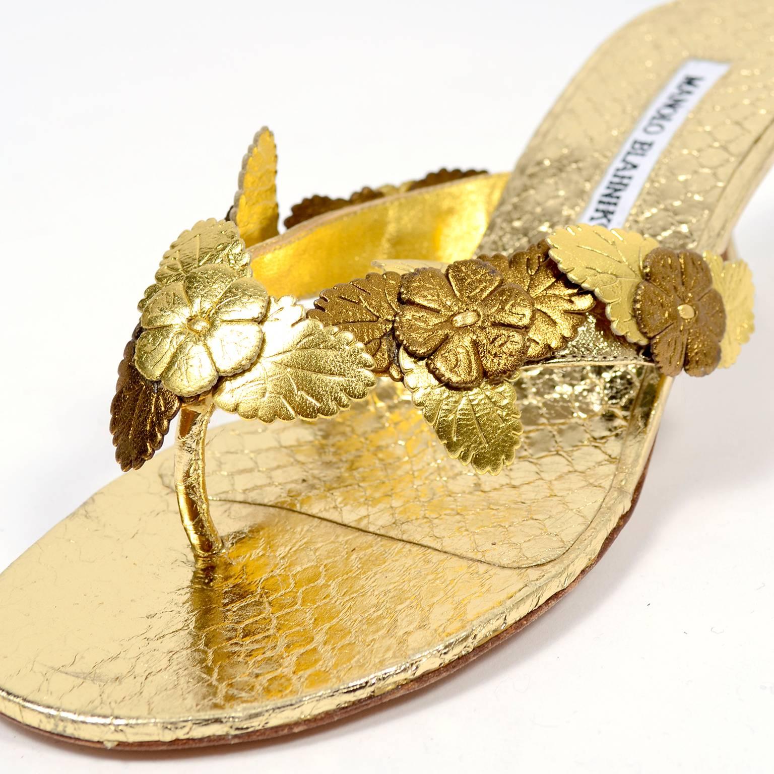 This is a pair of Manolo Blahnik shoes in a reptile embossed metallic gold leather with decorative cut flowers. These beautiful vintage Manolo Blahnik slip on shoes appear to have only been worn once and are labeled a size 37.  The shoes are sandal
