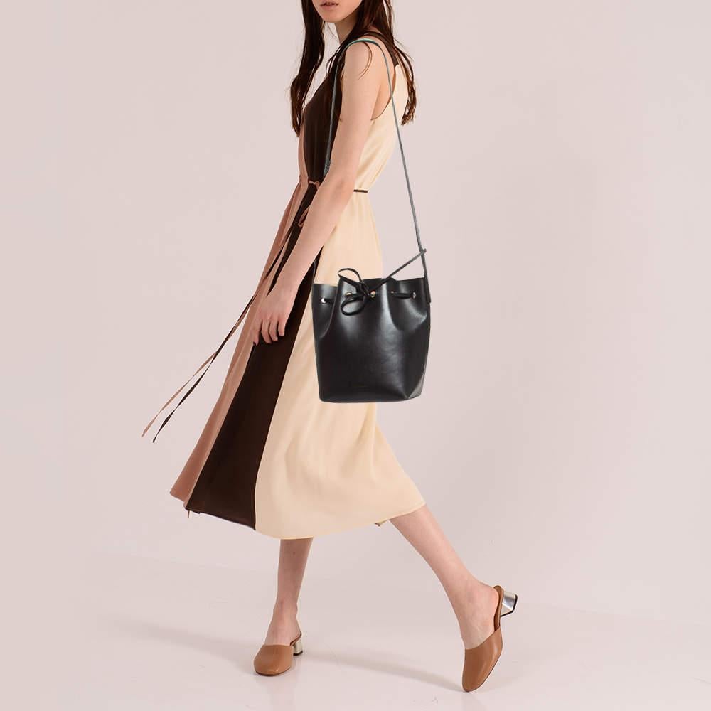 Este maravilloso diseño de Mansur Gavriel está fabricado en piel. El bolso tiene forma de cubo con un cierre de cordón que asegura el interior de piel. Se completa con una correa para el hombro. De color negro, es un accesorio adecuado para llevar