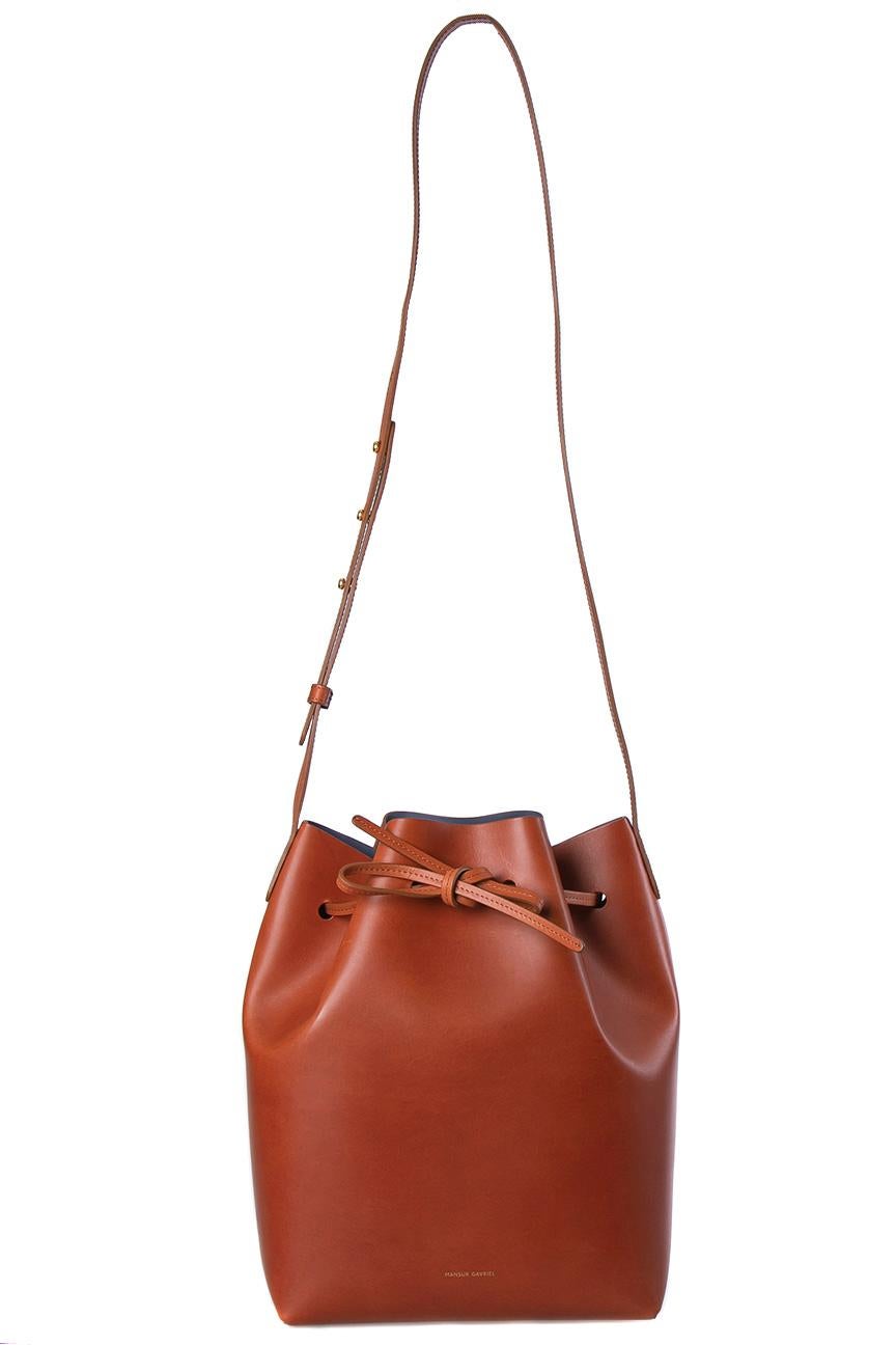 This wonderful Mansur Gavriel design is made from leather and enhanced with gold-tone hardware. The bag has a bucket shape with a drawstring closure that secures the leather interior. It is complete with a shoulder strap. Brown in color, it is an