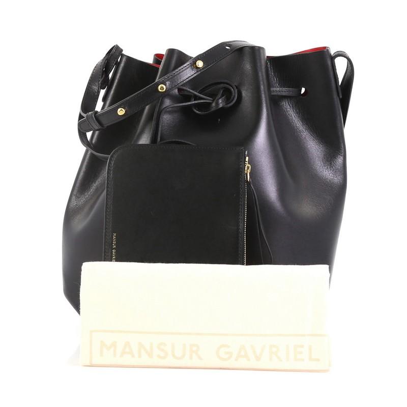 This Mansur Gavriel Bucket Bag Leather Large, crafted in black leather, features an adjustable leather shoulder strap and gold-tone hardware. Its drawstring closure opens to a red leather interior. 

Estimated Retail Price: $595
Condition: Very