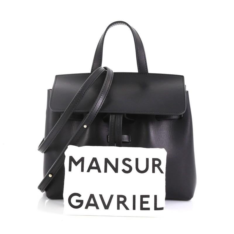 This Mansur Gavriel Lady Bag Leather Mini Mini, crafted in black leather, features a top flat leather handle, adjustable leather strap, gold-stamped logo at the front, and gold-tone hardware. Its hidden drawstring and magnetic closure opens to a red